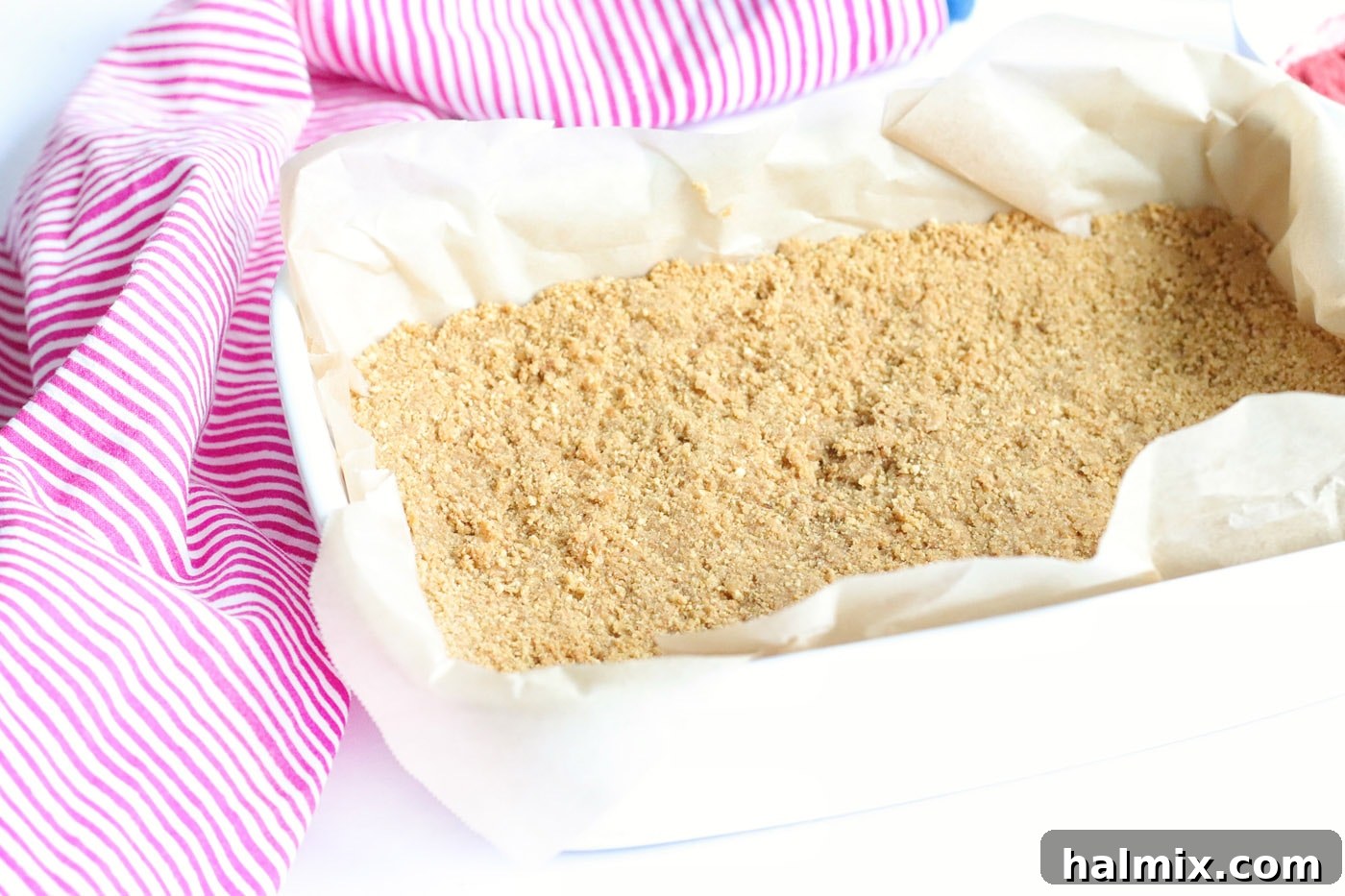 Graham cracker crumb crust pressed firmly into a parchment-lined baking dish.
