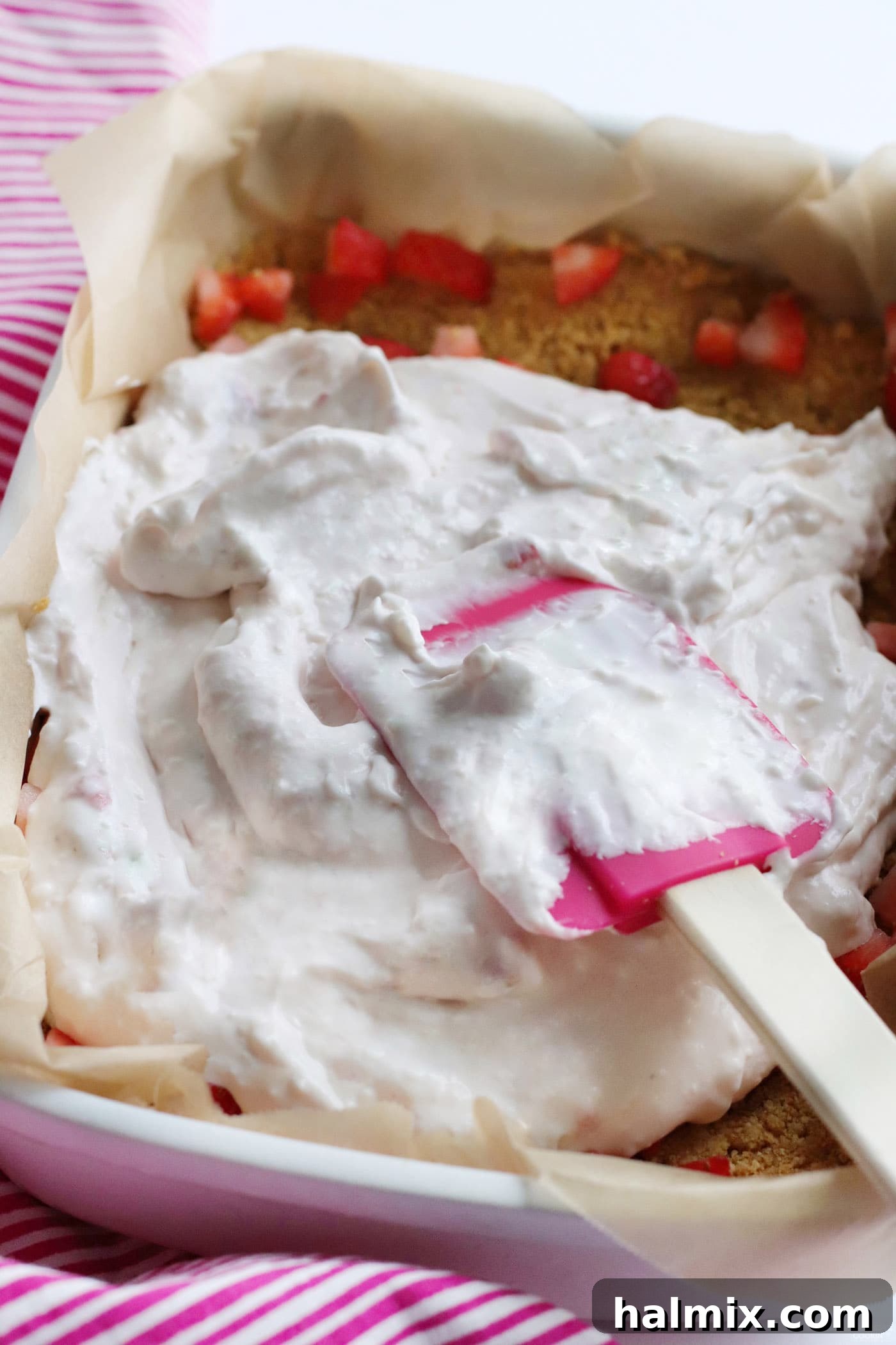 Spreading the creamy cheesecake filling layer smoothly on top of the fresh strawberries and graham cracker crust.