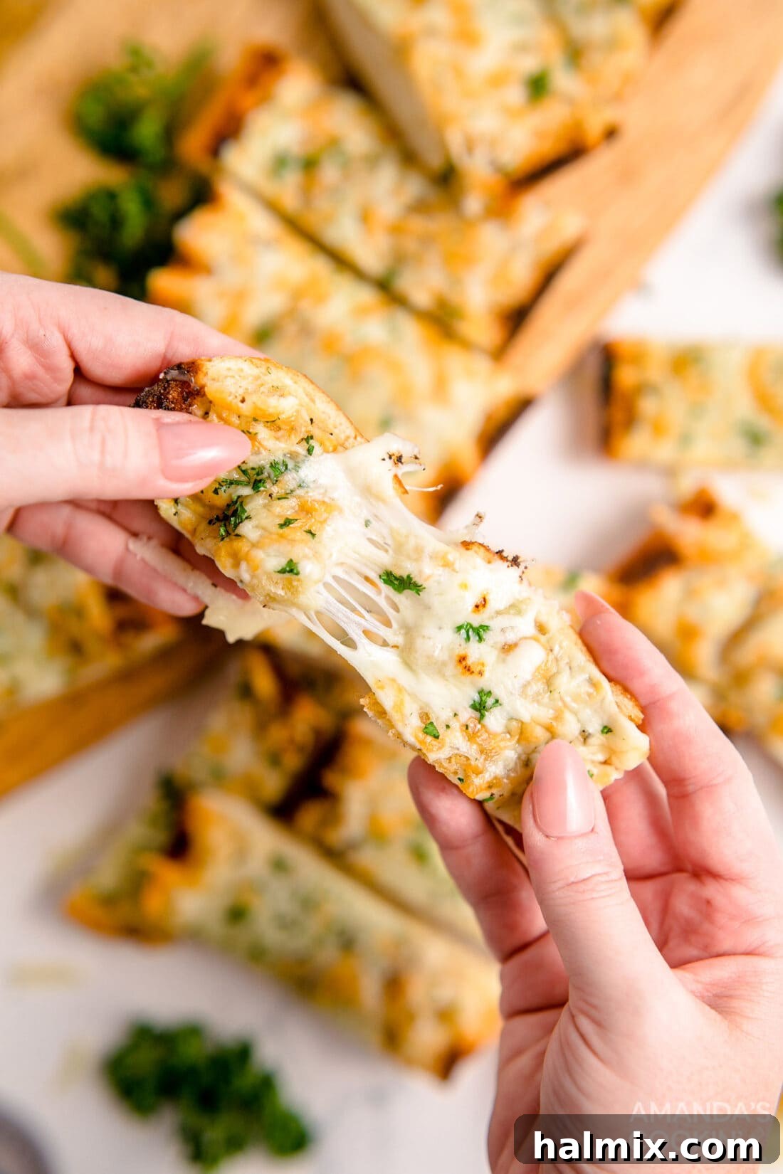 A hand pulling apart a piece of golden-brown Cheesy Garlic Bread, showing the melted mozzarella cheese stretch