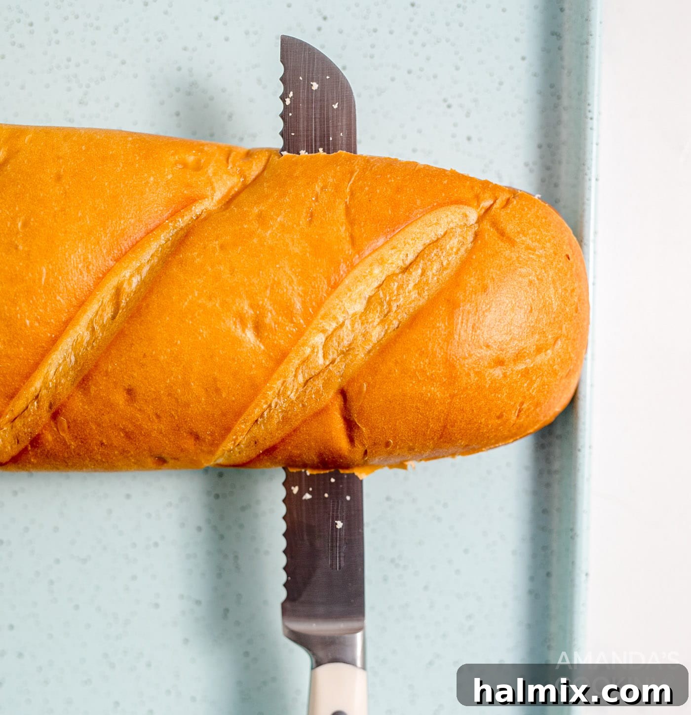 A knife slicing a French bread loaf in half lengthwise on a cutting board