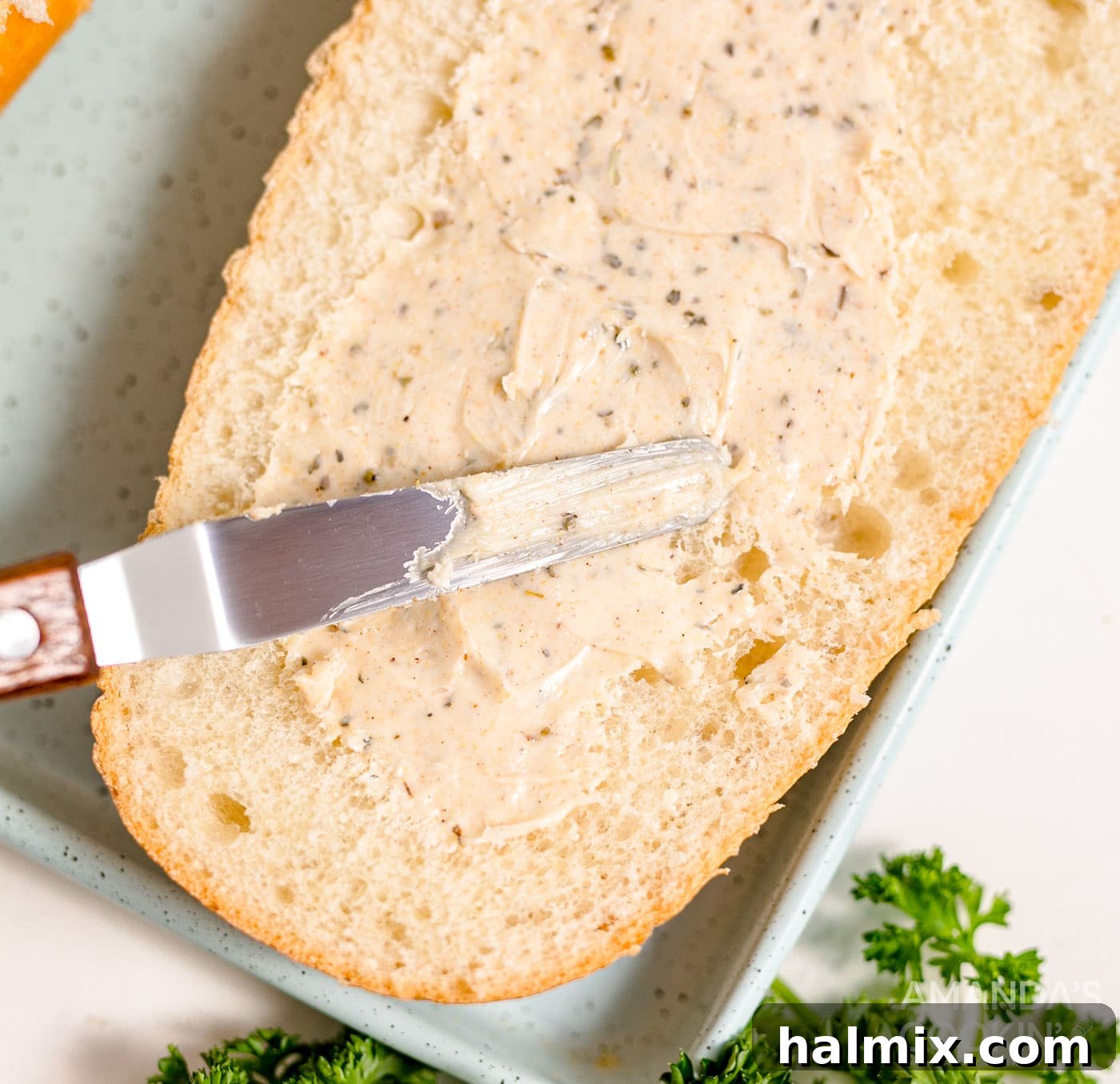 A butter knife spreading seasoned butter mixture onto a sliced French bread loaf