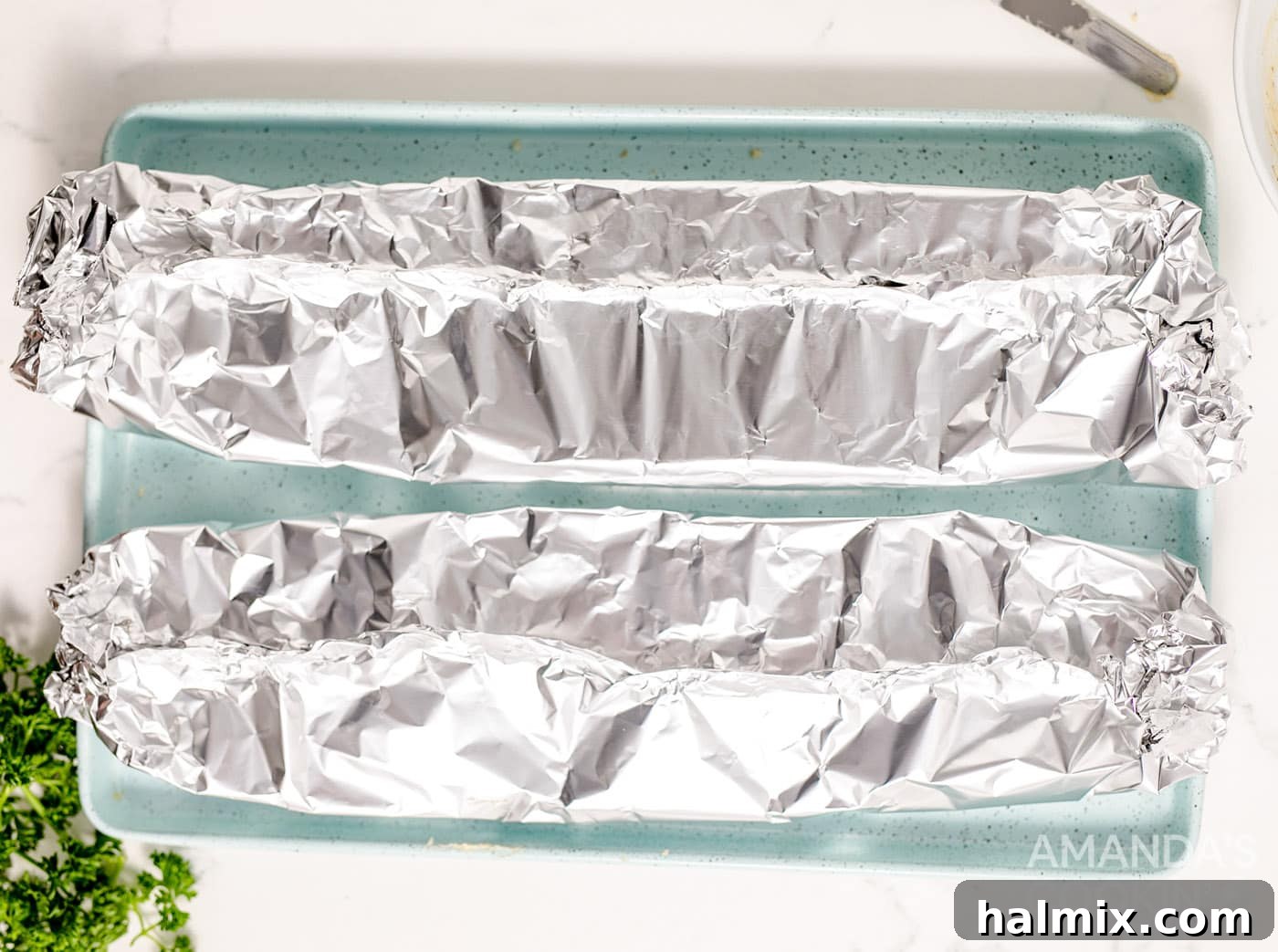 French bread halves wrapped in aluminum foil on a baking sheet