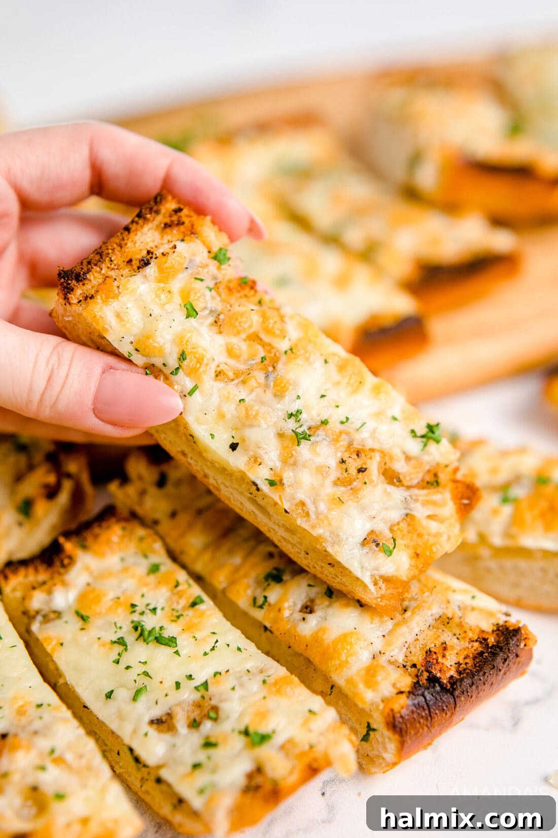 A hand reaching for a slice of warm, Cheesy Garlic Bread, demonstrating its appeal