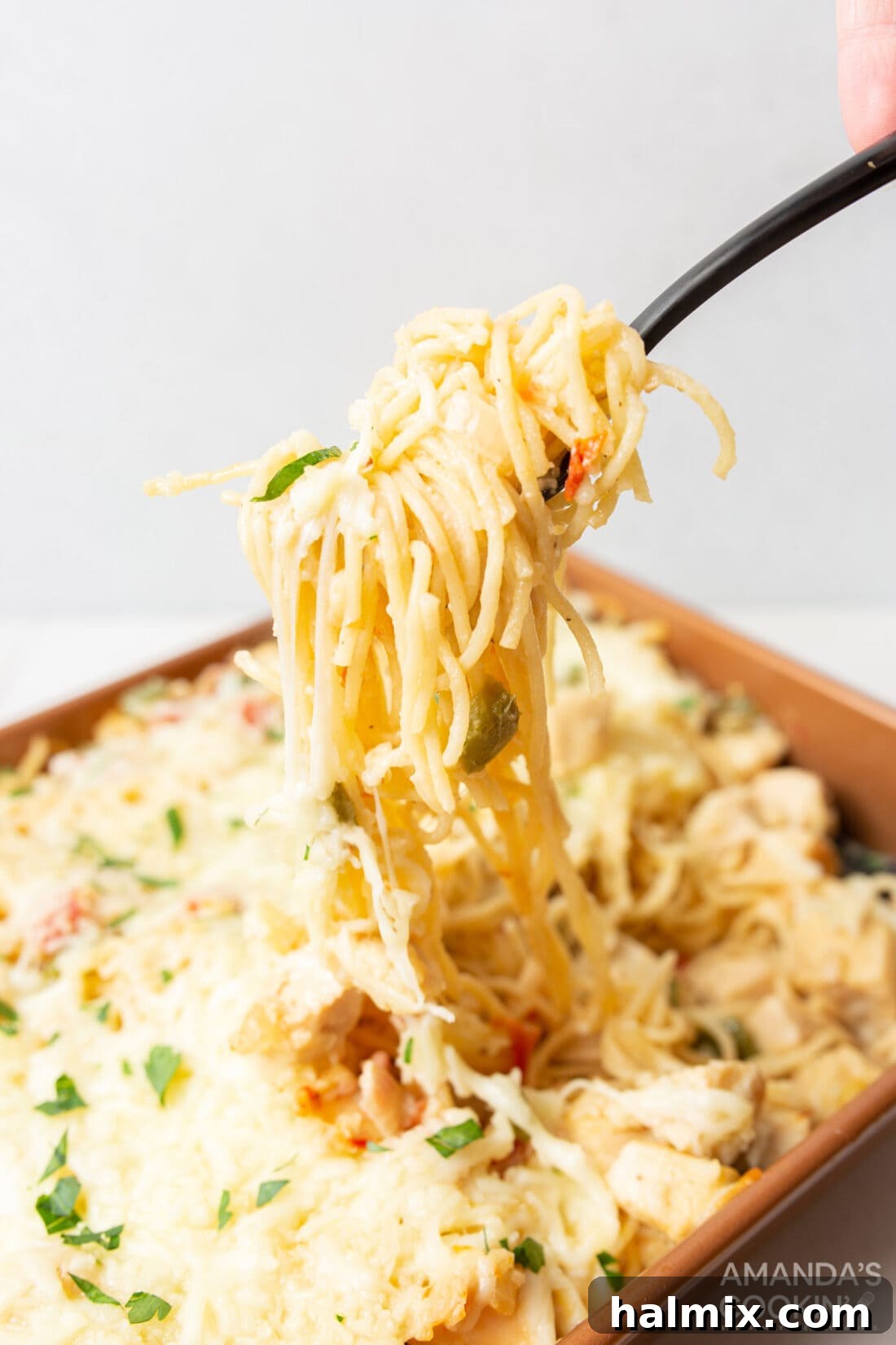 Lifting Cheesy Chicken Spaghetti with a serving fork, showing its creamy texture and melted cheese