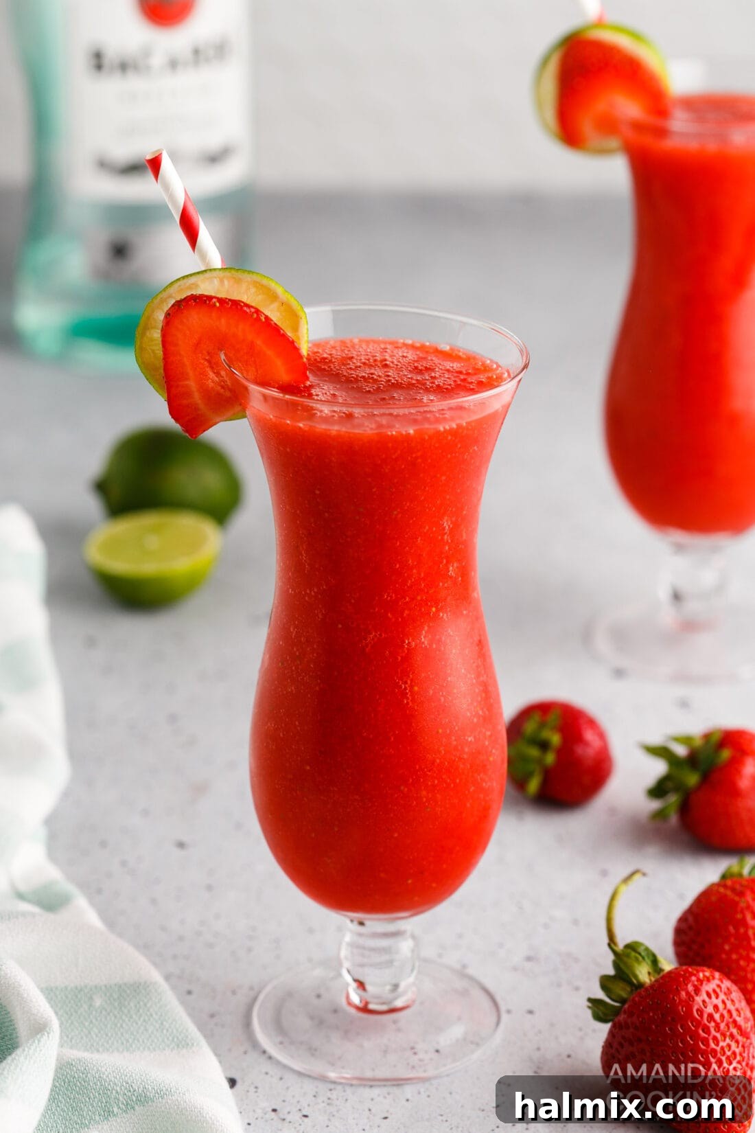 Vibrant Strawberry Daiquiri 2 Strawberry Daiquiri in a hurricane glass, garnished with a fresh strawberry and lime wedge.
