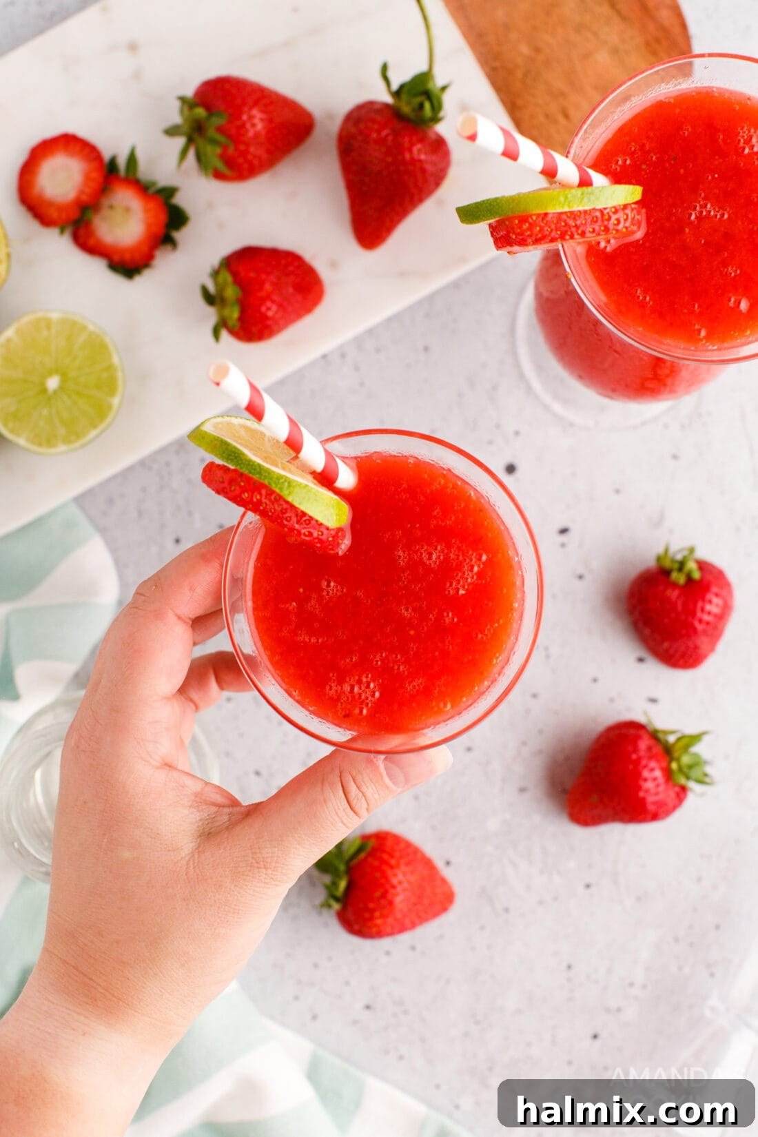 Vibrant Strawberry Daiquiri 7 A hand reaching for a perfectly chilled Strawberry Daiquiri garnished with a fresh strawberry and lime.