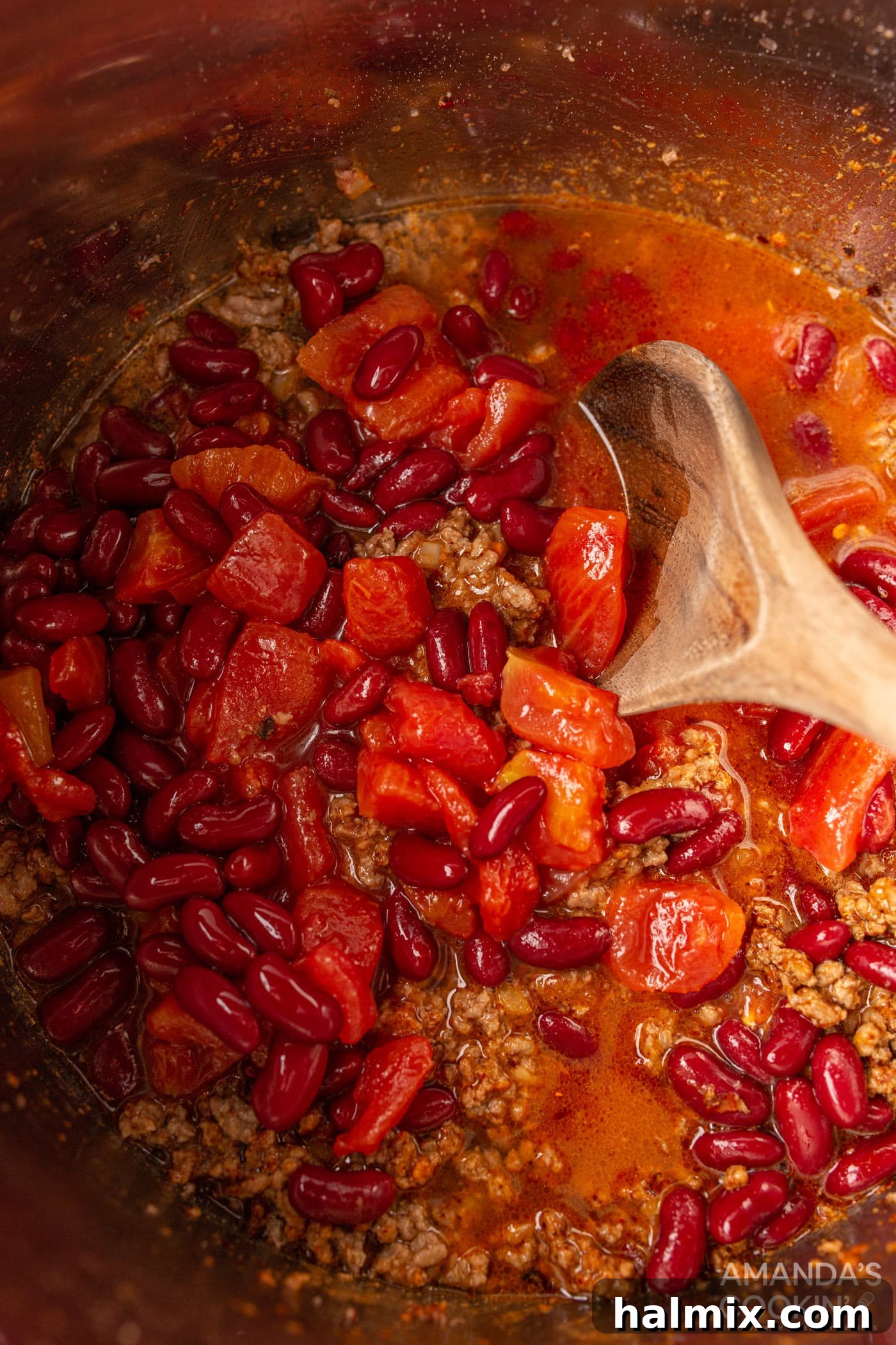 wooden spoon stirring tomatoes into chili