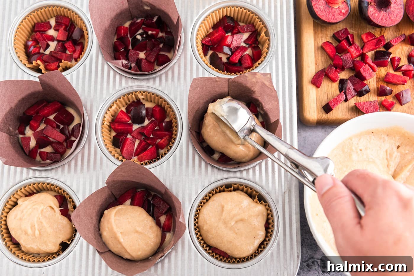 Scooping the remaining muffin batter over the chopped plums in the muffin pan, creating a second layer.