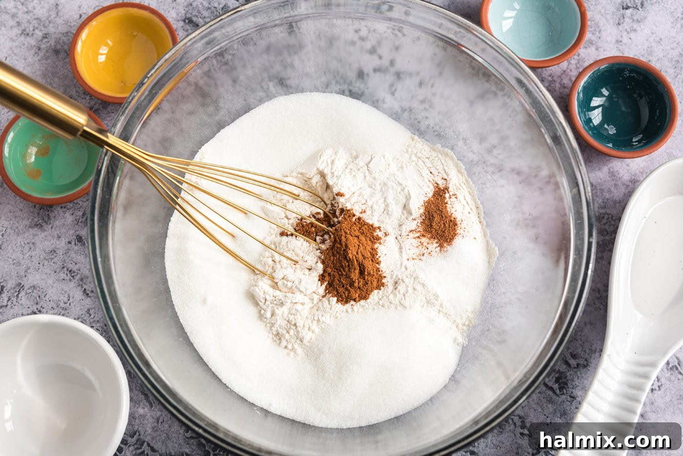 Golden Sugar Plum Muffins 5 A bowl containing a mixture of dry ingredients: sugar, cinnamon, flour, nutmeg, and baking powder, with a whisk resting inside.