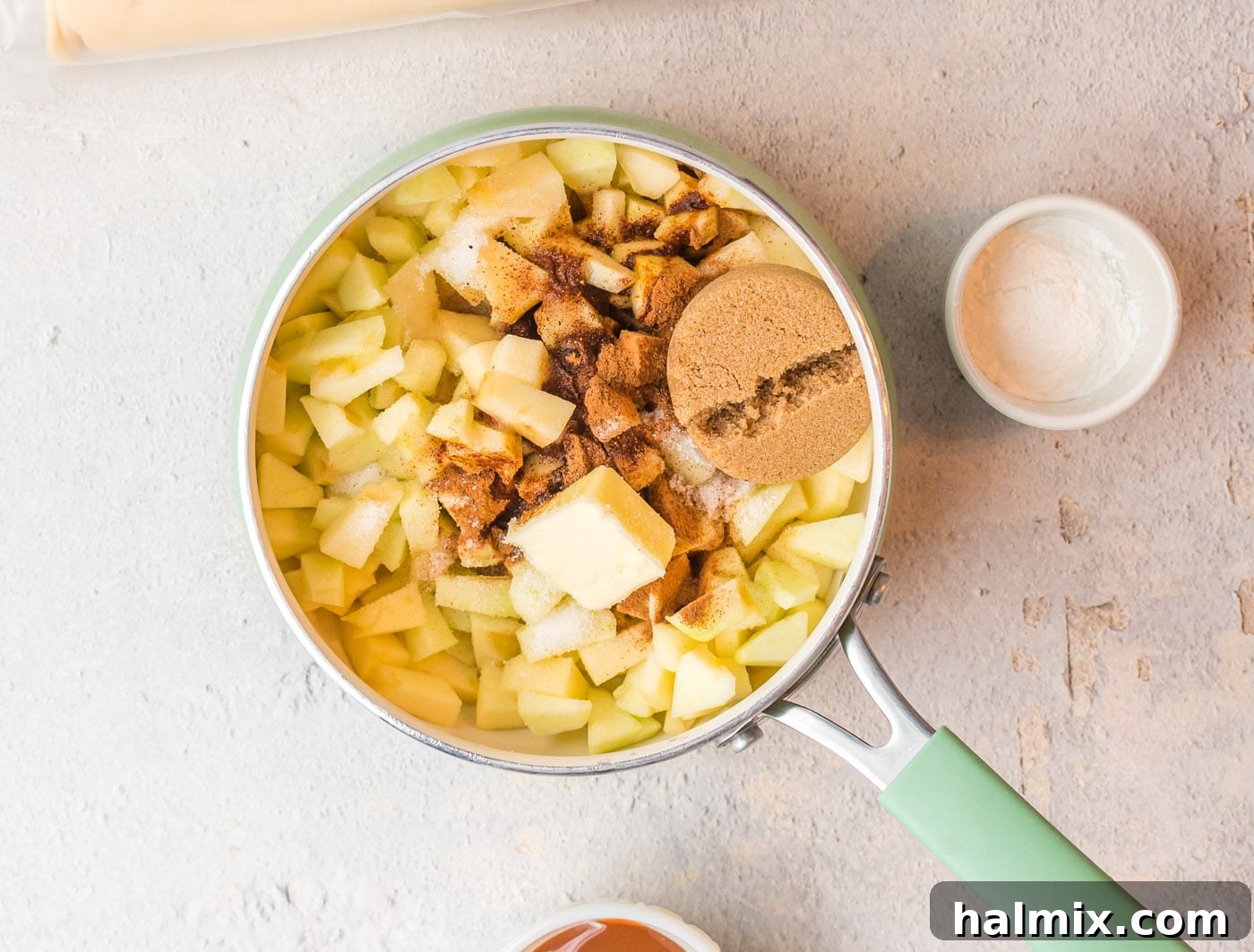 Diced apples, spices, butter, and sugars being combined in a saucepan, beginning the cooking process for the hand pie filling.