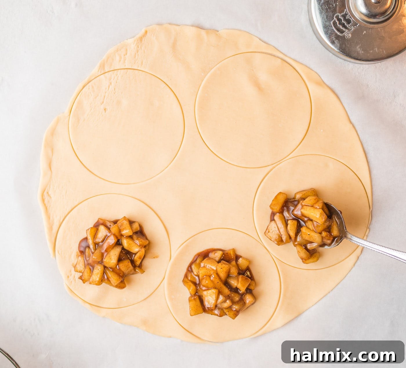 Apple filling being carefully placed onto a pie crust circle, ensuring it's centered and not overfilled.