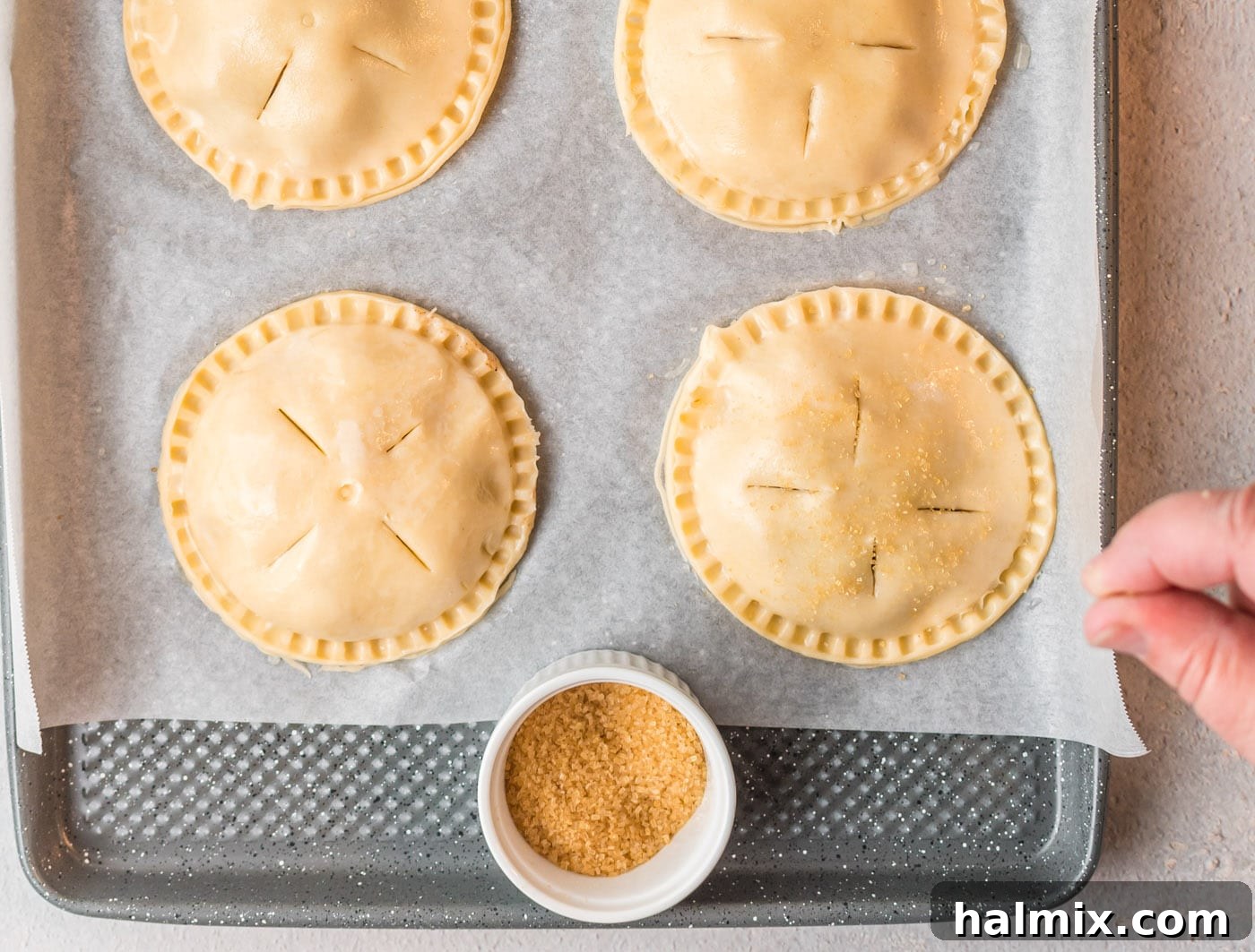 Apple hand pies meticulously brushed with egg wash and sprinkled with sugar, perfectly prepped and ready for baking.