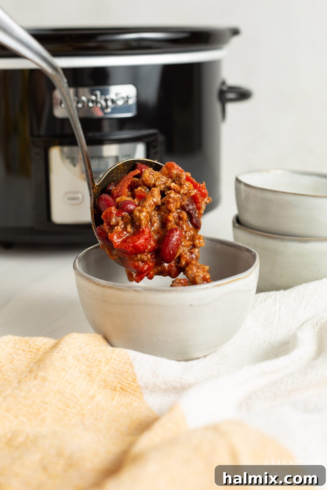 A large serving spoon dishing out Crockpot Chili into a bowl.