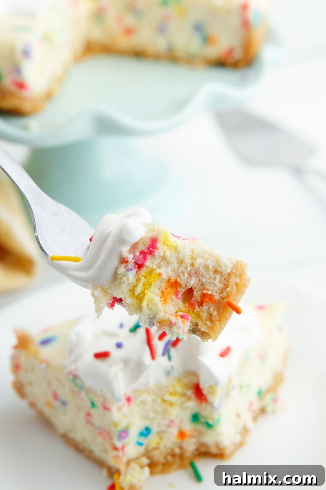 A fork taking a bite from a slice of Instant Pot Funfetti Cheesecake, showing its creamy texture and colorful sprinkles.