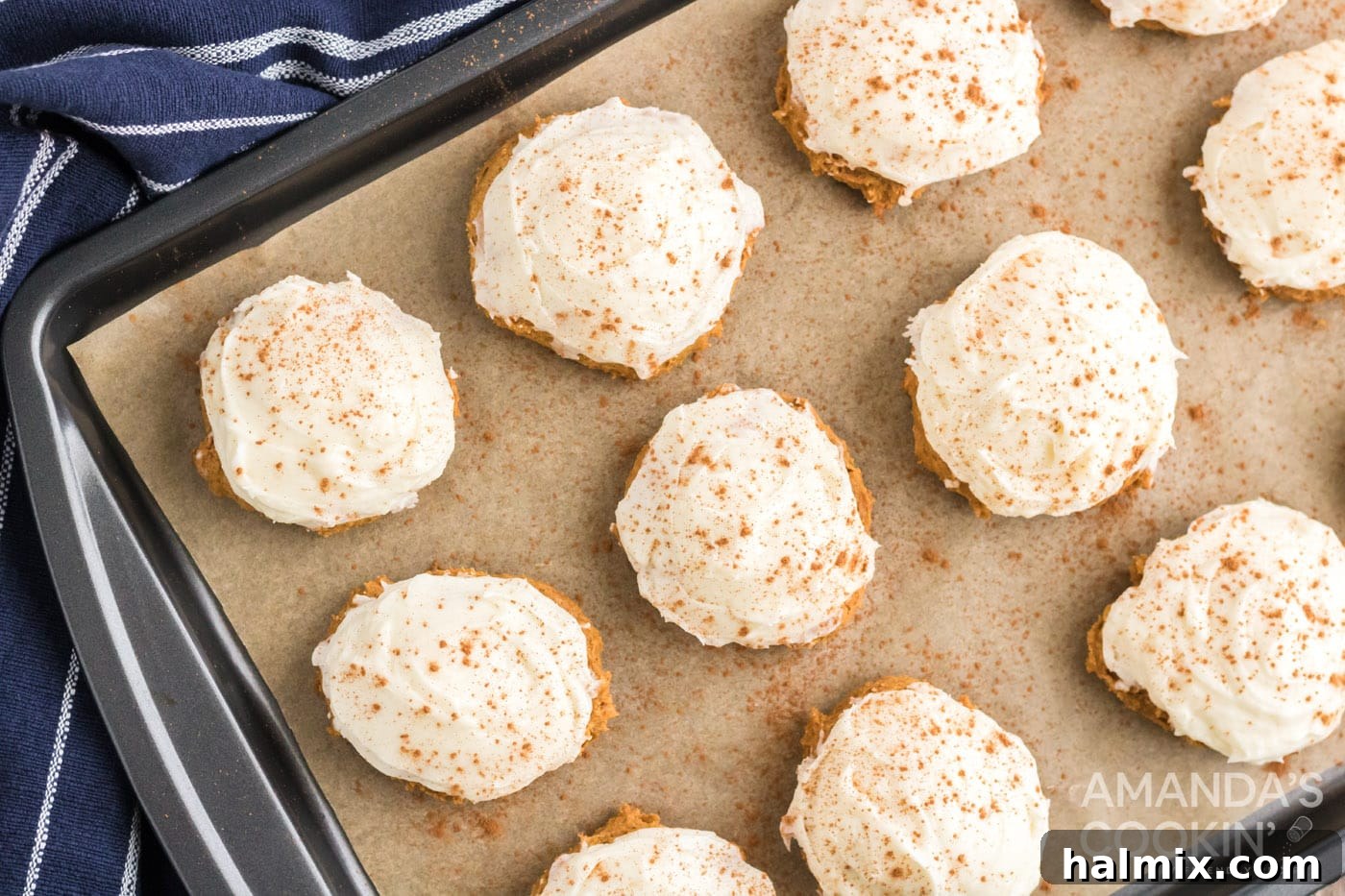 Delicious Pumpkin Cake Mix Treats 9 Cream cheese frosting generously spread on top of pumpkin cake mix cookies arranged on a baking sheet, with a dusting of cinnamon.