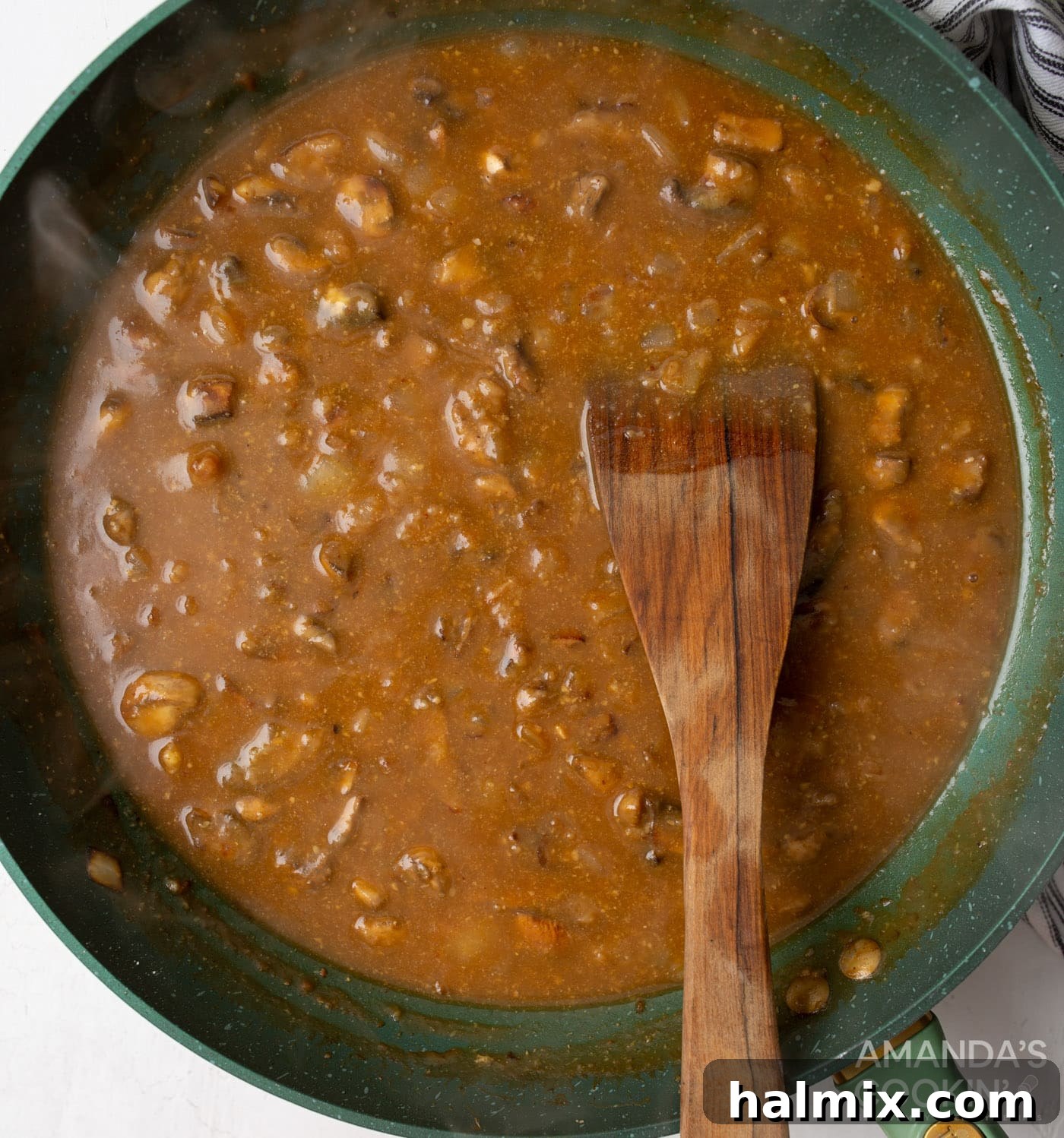 Creamy Beef Noodle Bake 7 Beef stock being poured into a skillet with sautéed mushrooms and onions coated in flour, forming a roux.