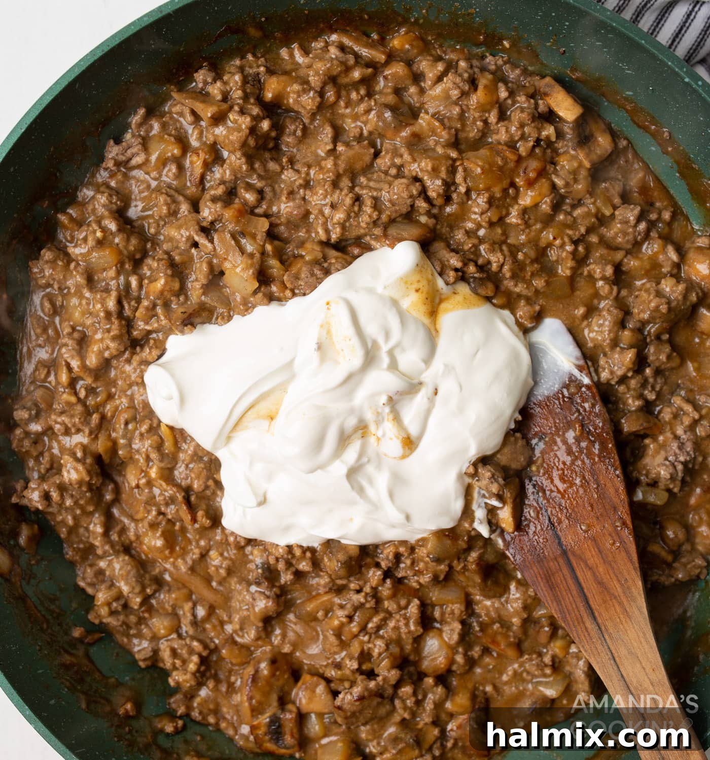 Creamy Beef Noodle Bake 8 Sour cream being stirred into the ground beef stroganoff mixture in a skillet, creating a creamy texture.