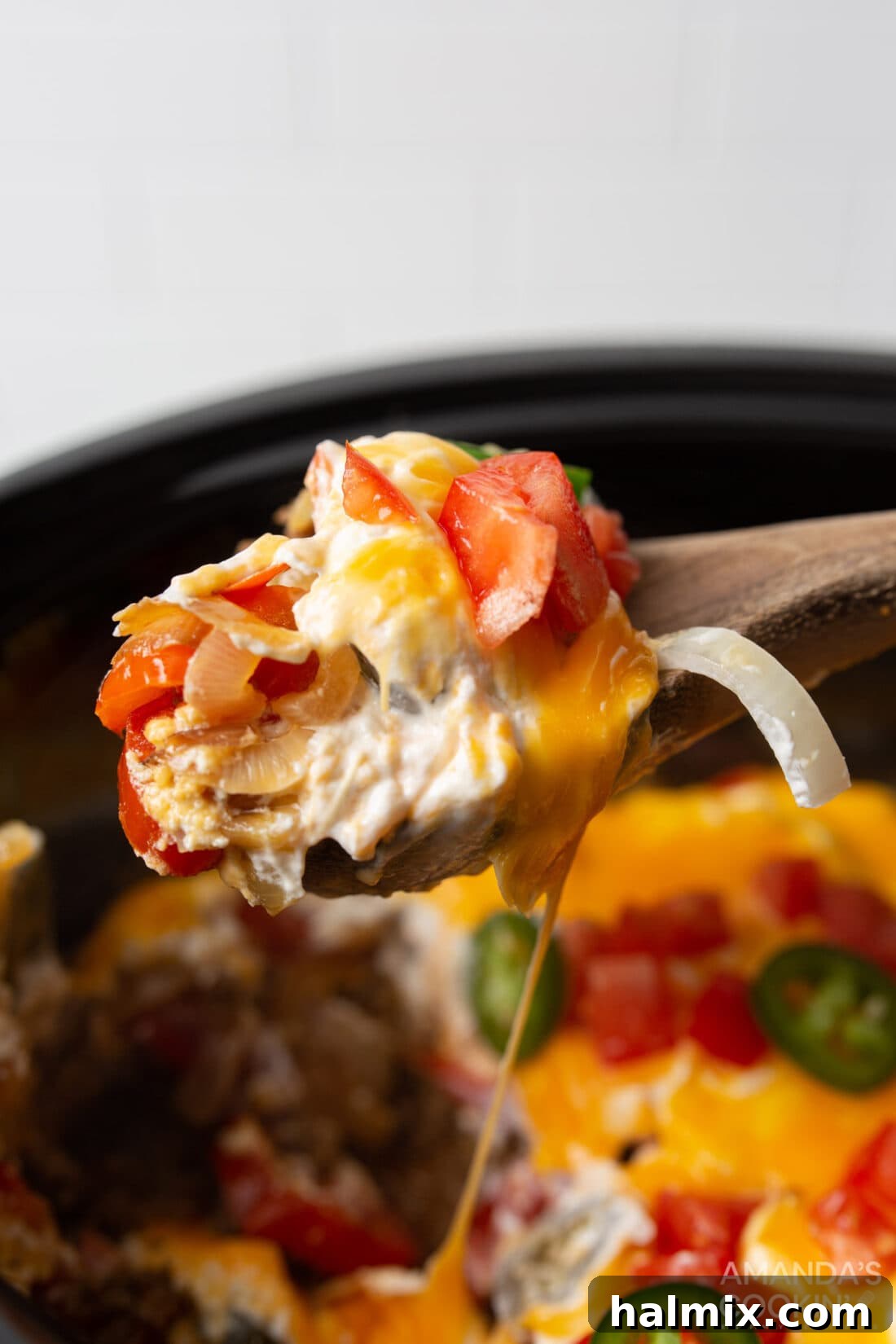 A serving spoon lifting a portion of the rich and creamy Crockpot John Wayne Casserole from the slow cooker, showcasing its layers.