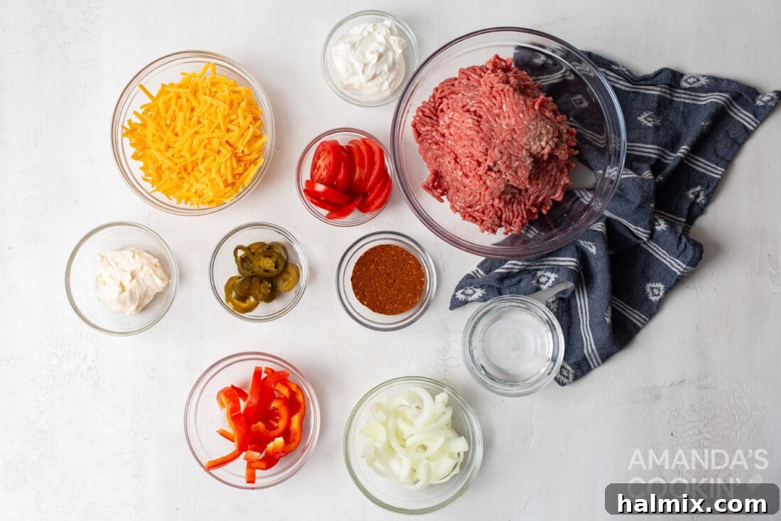 A collection of fresh ingredients laid out, including ground beef, onions, bell peppers, tomatoes, jalapenos, sour cream, mayonnaise, and shredded cheddar cheese, prepared for Crockpot John Wayne Casserole.