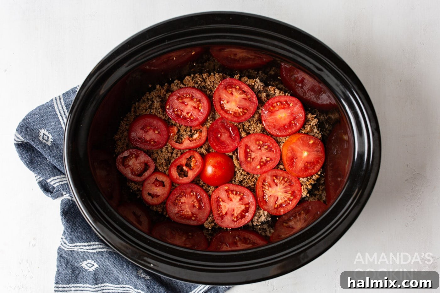 Sliced tomatoes carefully placed on top of the seasoned ground beef layer in the crockpot.