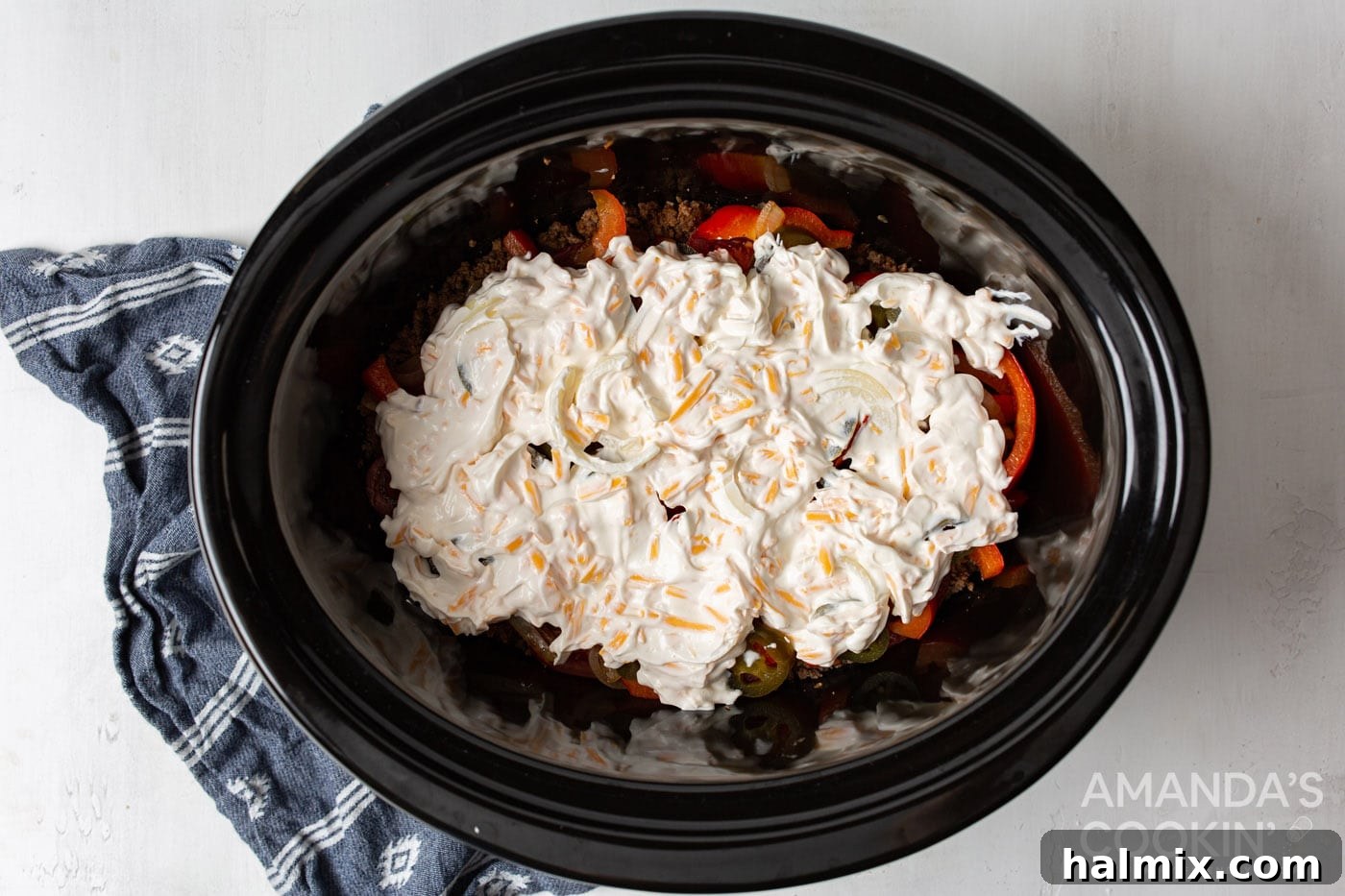 The creamy sour cream mixture spread evenly over the ground beef and vegetable layers in the slow cooker.