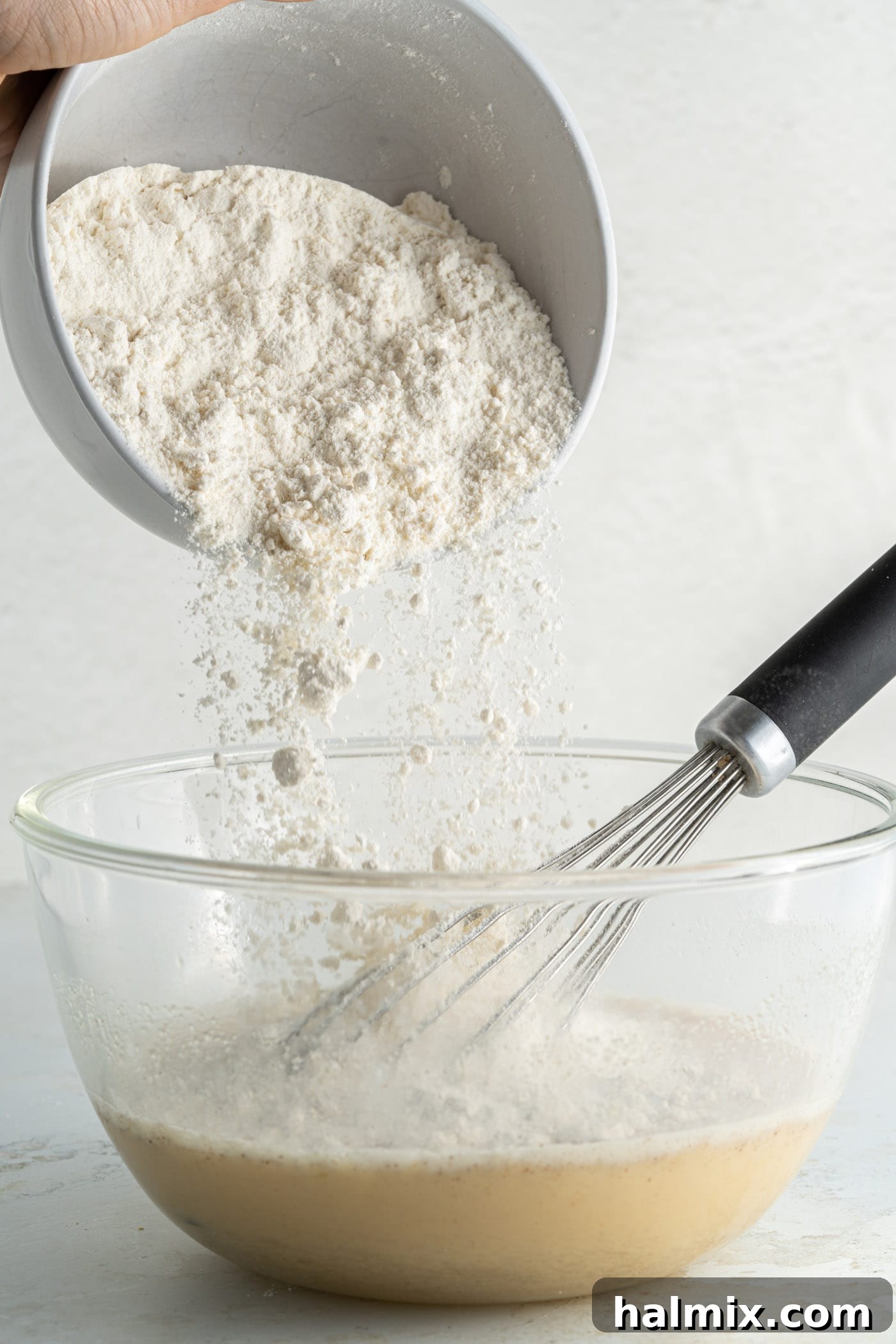 adding flour to pancake batter in a bowl