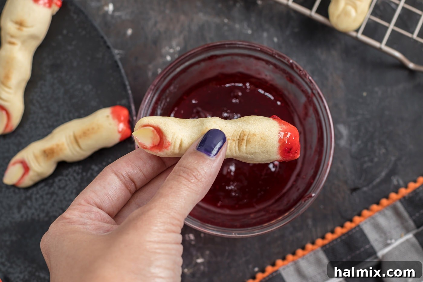 Hexed Hand Delights 16 A witch finger cookie being dipped into a bowl of strawberry jam, creating a convincing 'severed and bloody' effect.