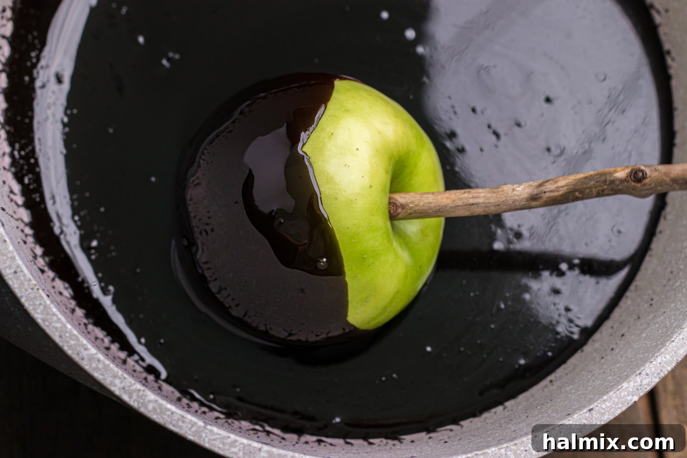 An apple being dipped into the glossy black candy coating.