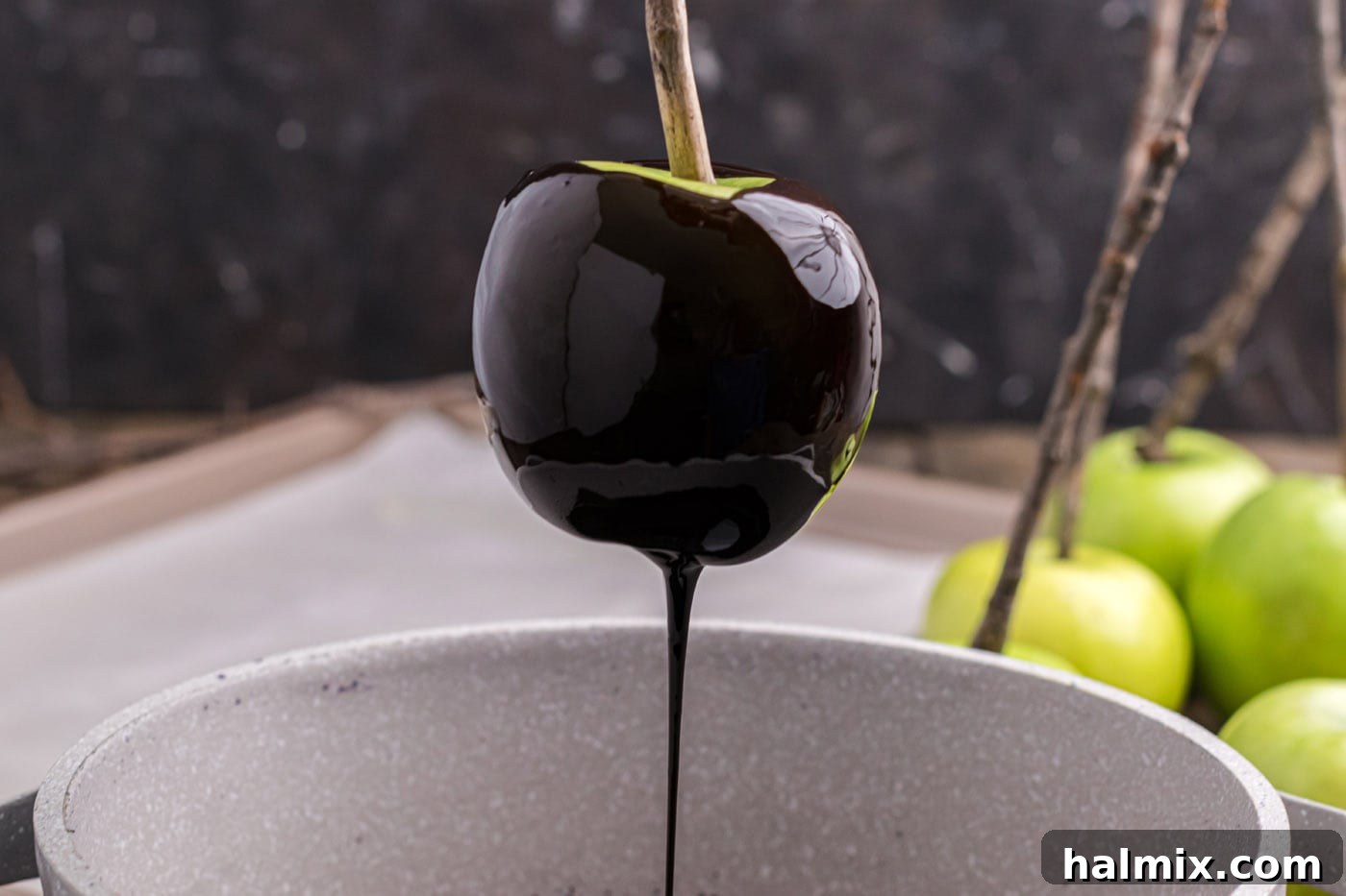 Excess black candy coating dripping off a freshly dipped apple.