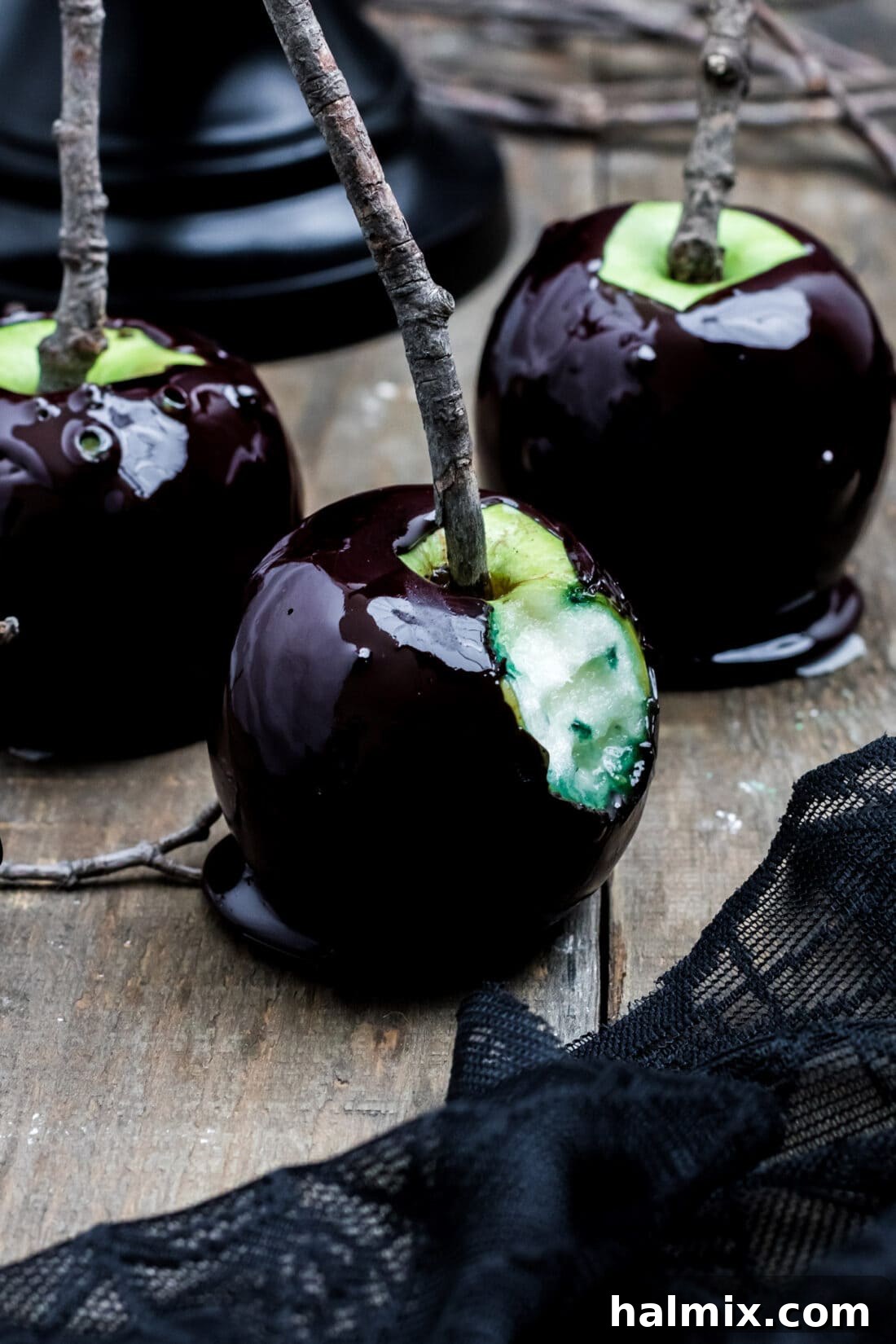 A black Halloween candy apple with a bite taken out of it, revealing the green apple underneath.