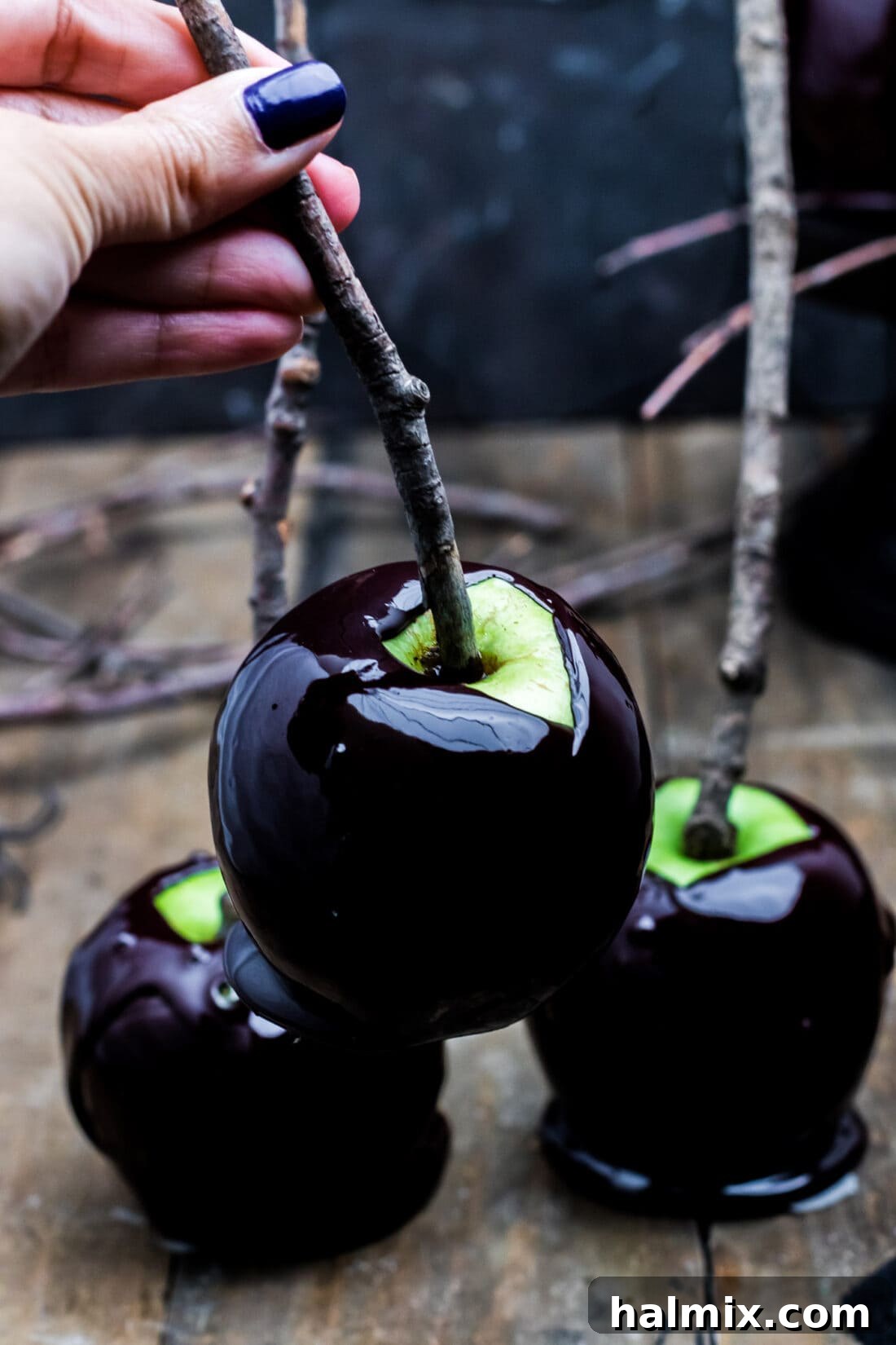 A hand lifting a perfectly coated black Halloween candy apple, showcasing its glossy finish.