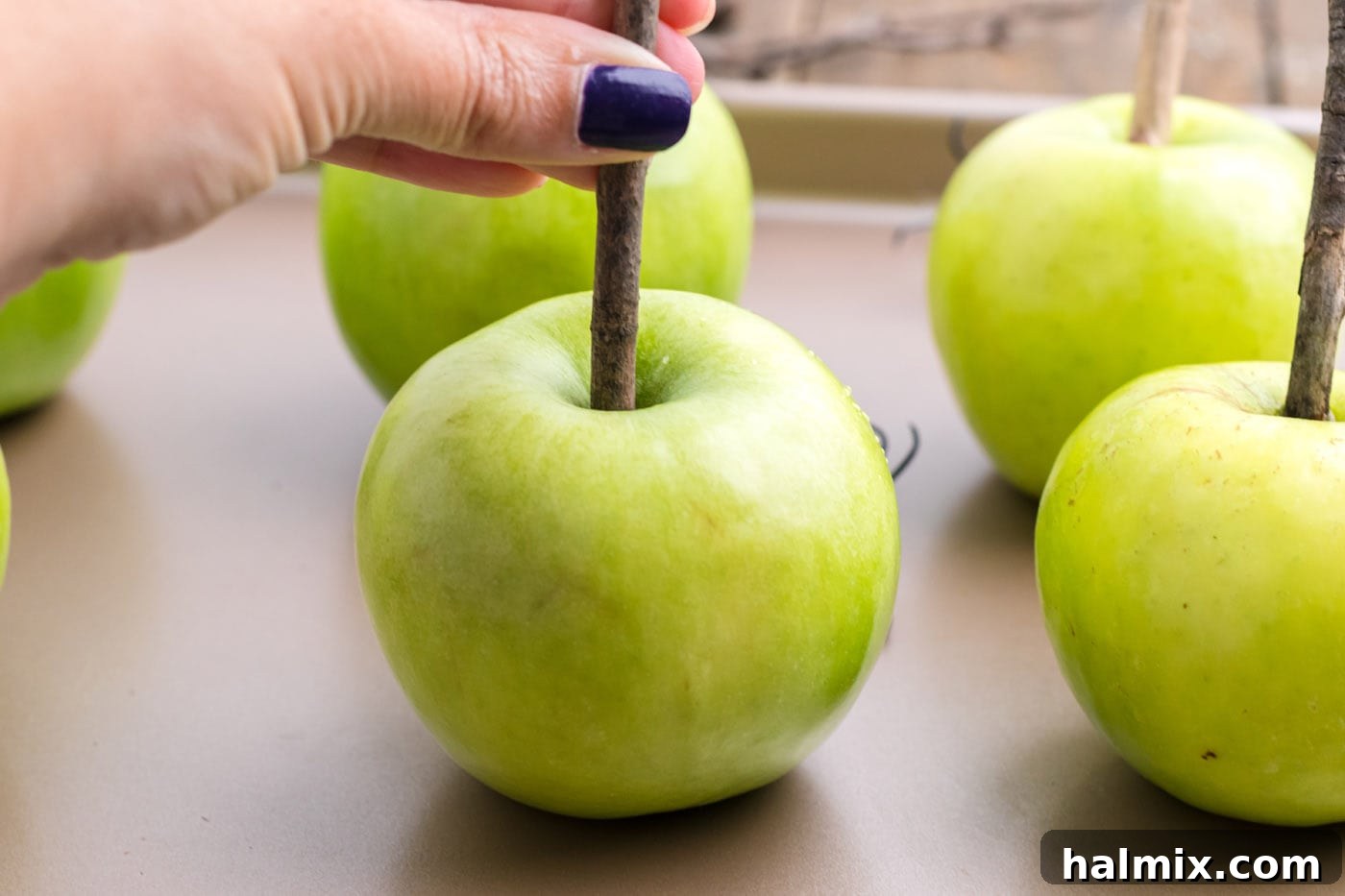 A hand inserting a natural wood stick into a green apple.