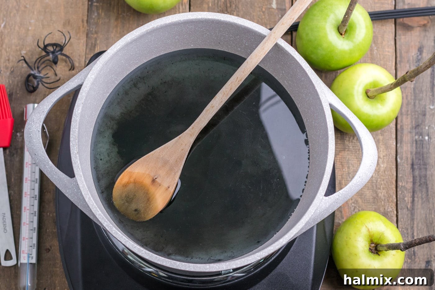 Sugar, corn syrup, water, and black gel food coloring in a saucepan, being mixed.