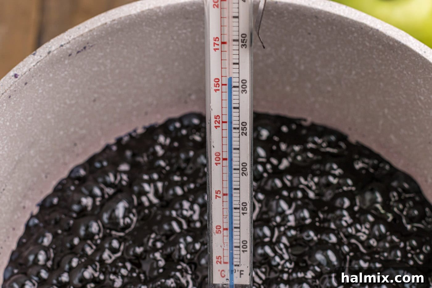A candy thermometer immersed in the black candy apple coating mixture, indicating temperature.