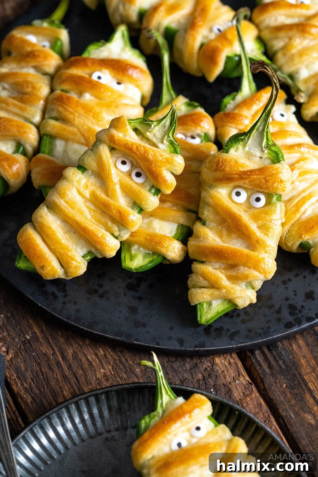 Jalapeno Popper Mummies on a black plate, ready for a Halloween party