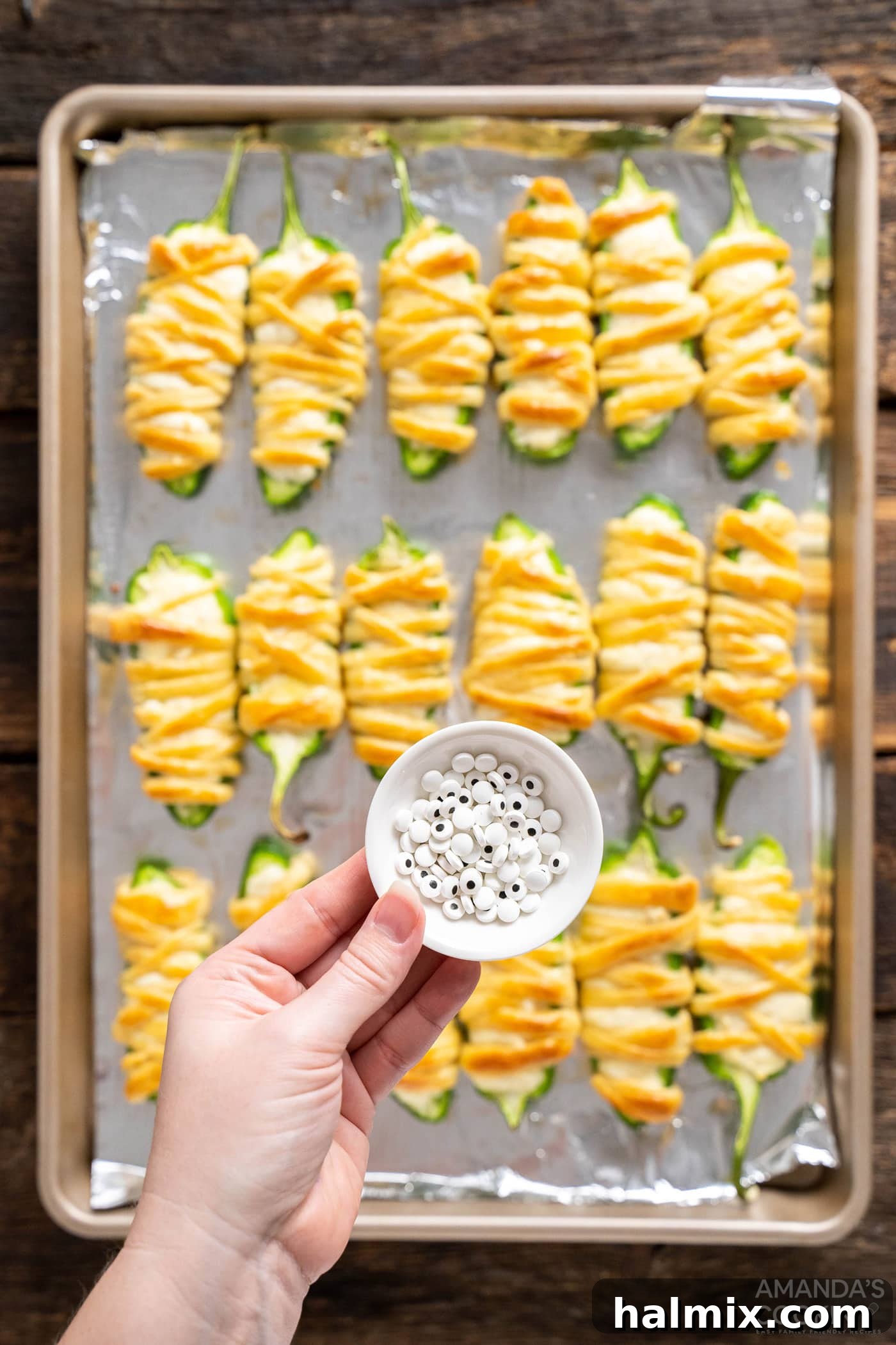 Candy eyeballs placed over jalapeno popper mummies on a baking sheet, giving them a spooky appearance