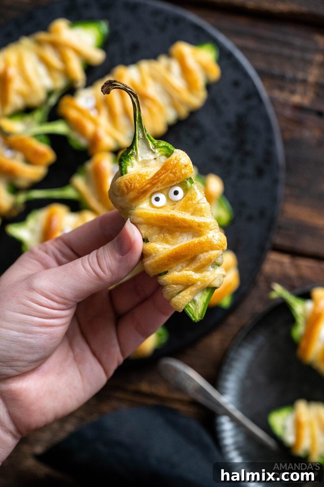 Hand holding a single Jalapeno Popper Mummy, showing its detail and enticing appearance
