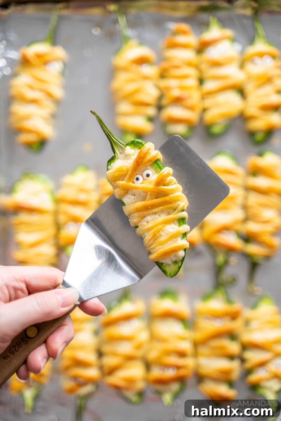Spatula holding a freshly baked Jalapeno Popper Mummy, showcasing its golden crust and creamy filling
