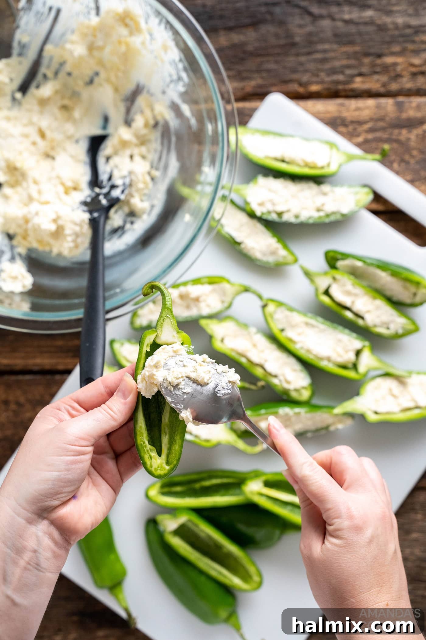 Spoonful of cream cheese mixture being stuffed into jalapeno halves, ready for wrapping