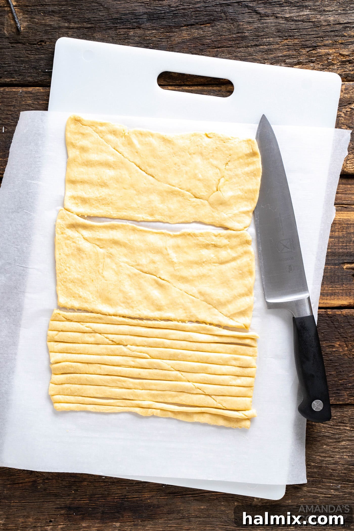 Sliced crescent dough on a cutting board, prepared into thin strips for wrapping the jalapenos