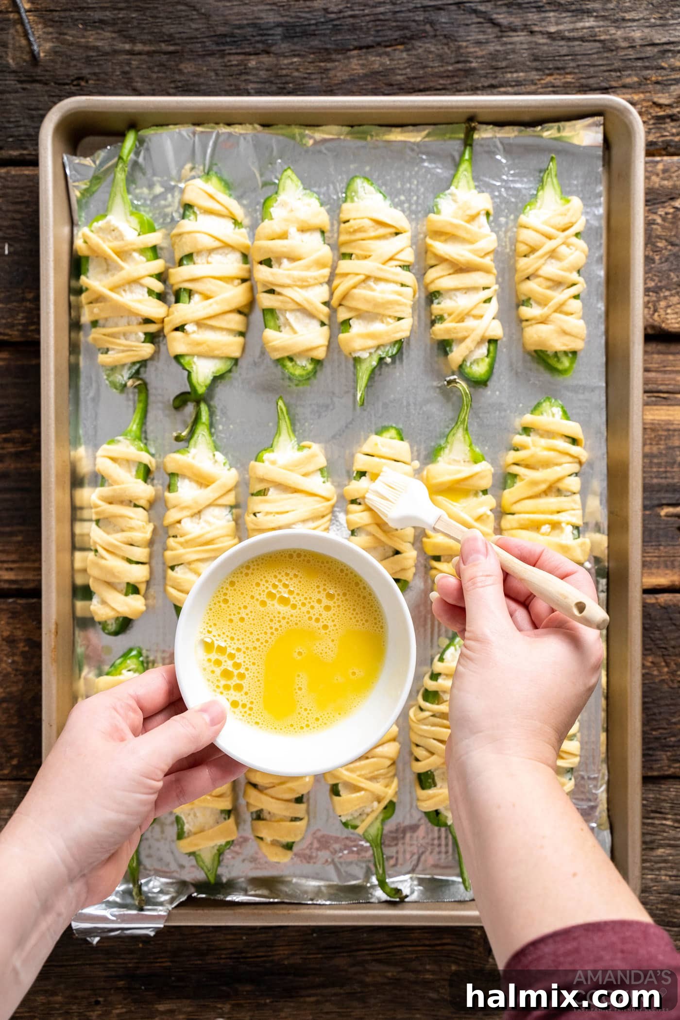 Brushing egg wash on jalapeno poppers arranged on a baking sheet, ready for the oven
