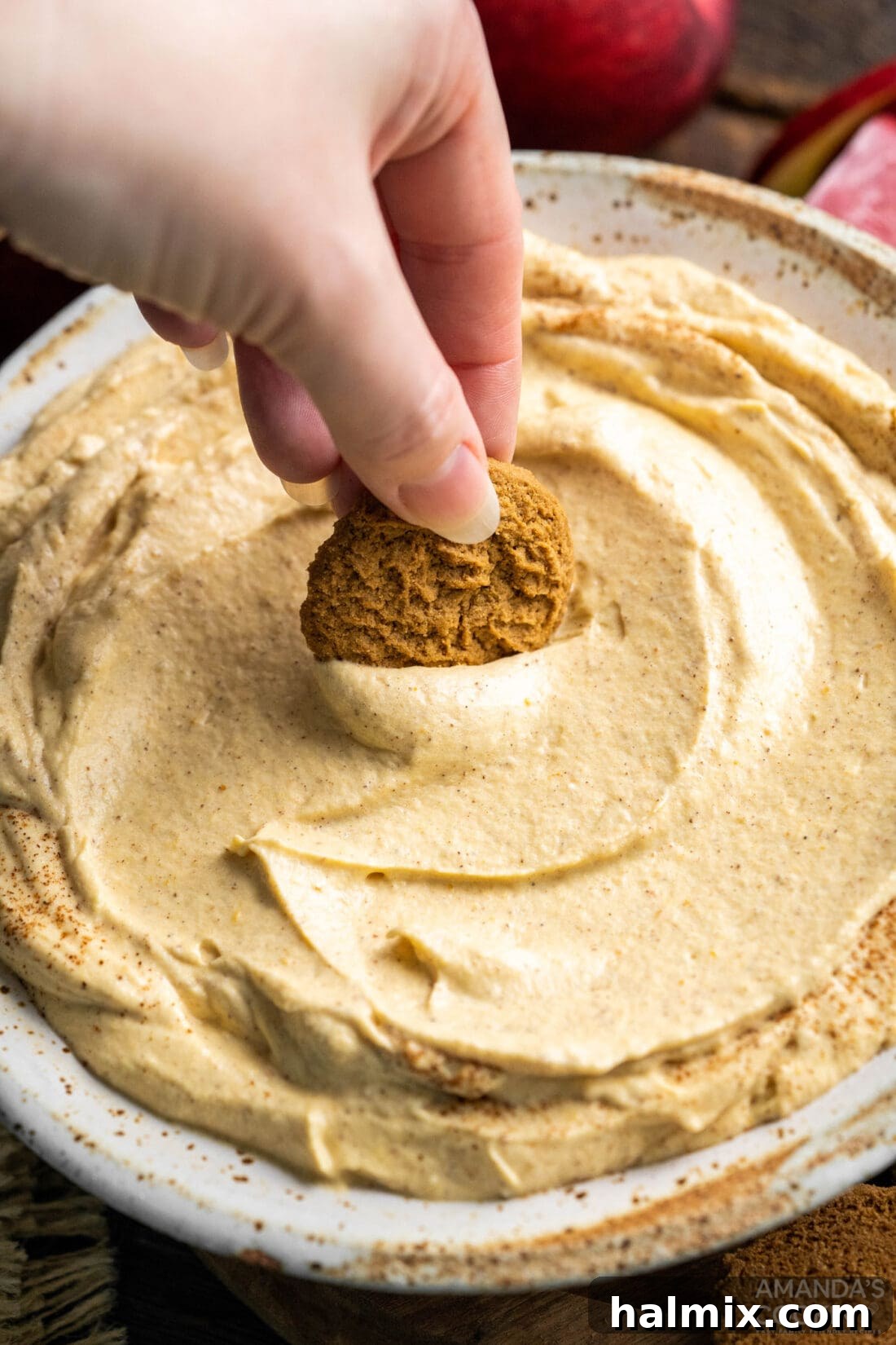 A close-up shot of a cookie being dipped into a luscious bowl of No-Bake Pumpkin Pie Dip, highlighting its smooth and inviting texture.