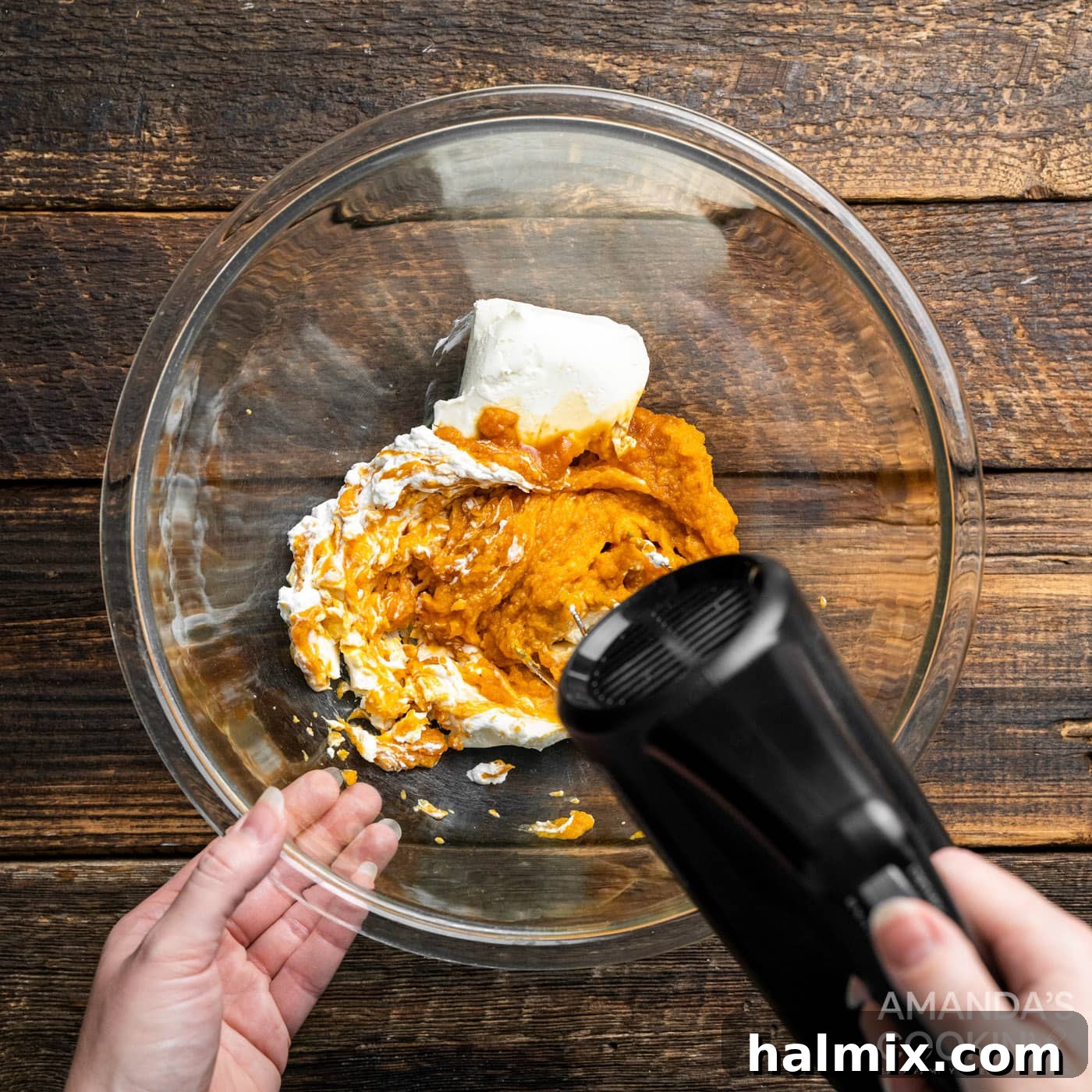 A handheld electric mixer actively blending smooth cream cheese and vibrant pumpkin puree in a large bowl, creating the foundational base for the dip.
