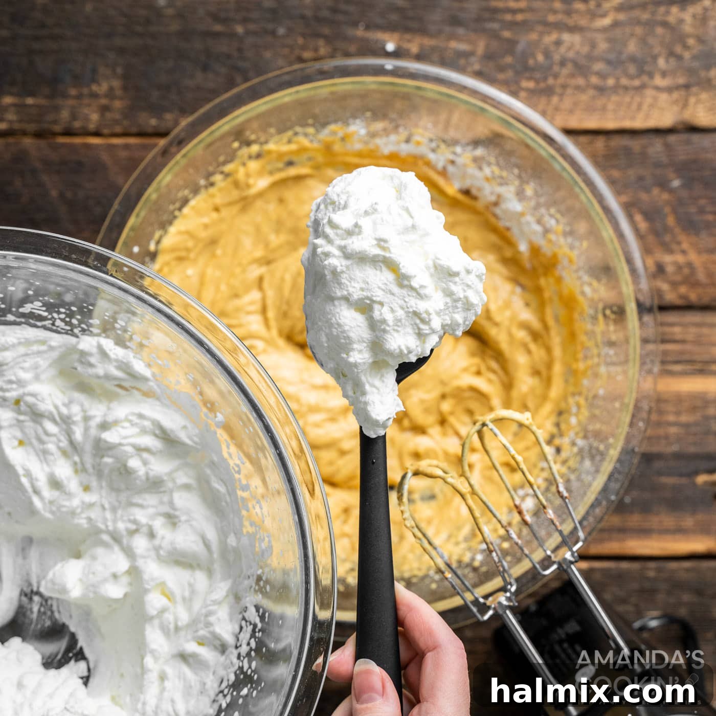 A spoonful of freshly whipped cream delicately resting atop the rich pumpkin and cream cheese mixture in the bowl, poised for gentle incorporation.