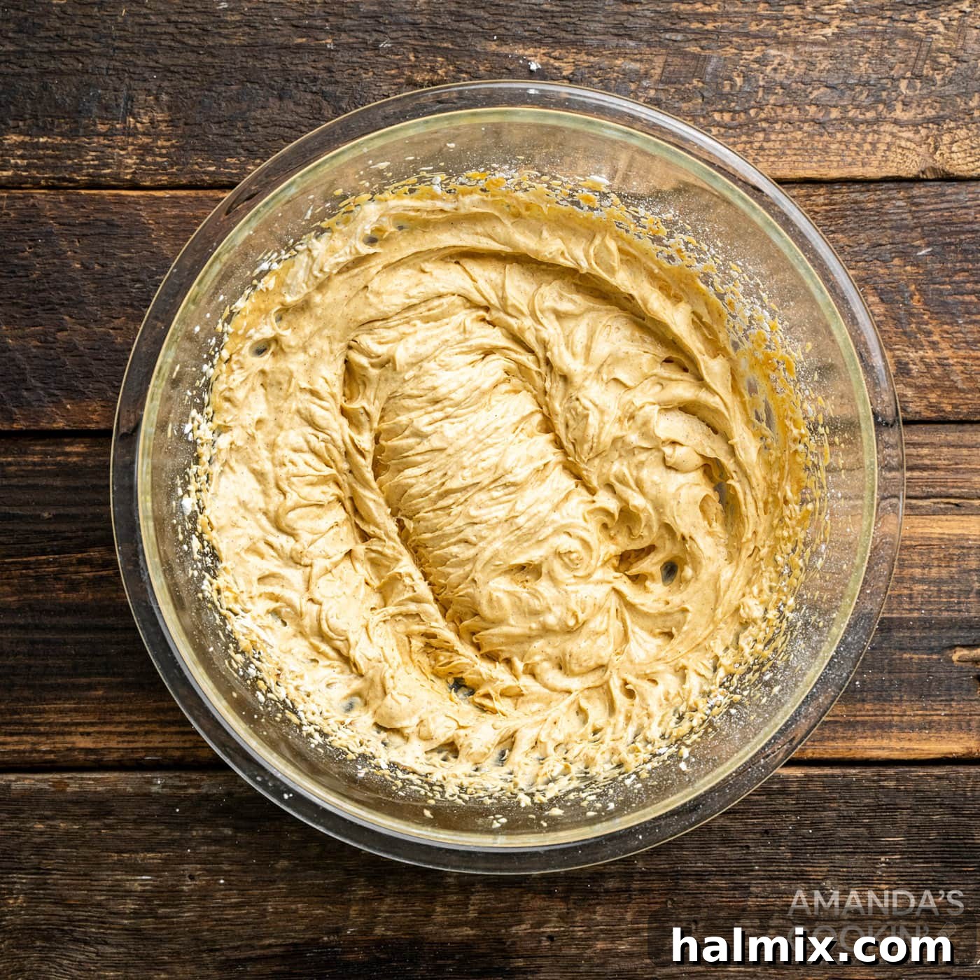 The whipped cream has been partially folded into the pumpkin and cream cheese mixture, creating a swirl of light and darker hues within the bowl, indicating a creamy, evolving consistency.