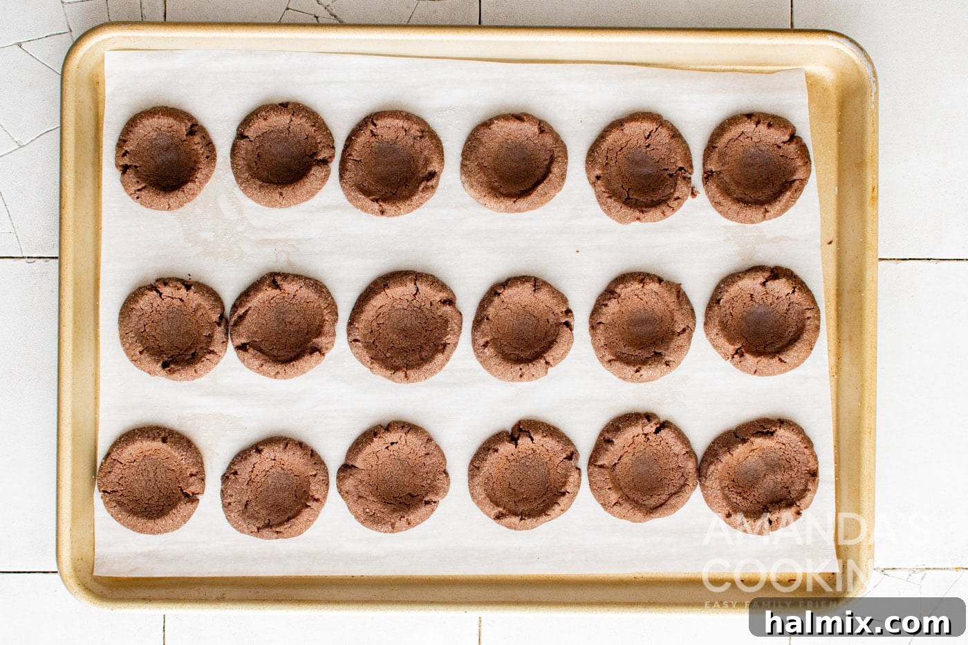 baked chocolate thumbprint cookies on a cookie sheet, with divots reformed.