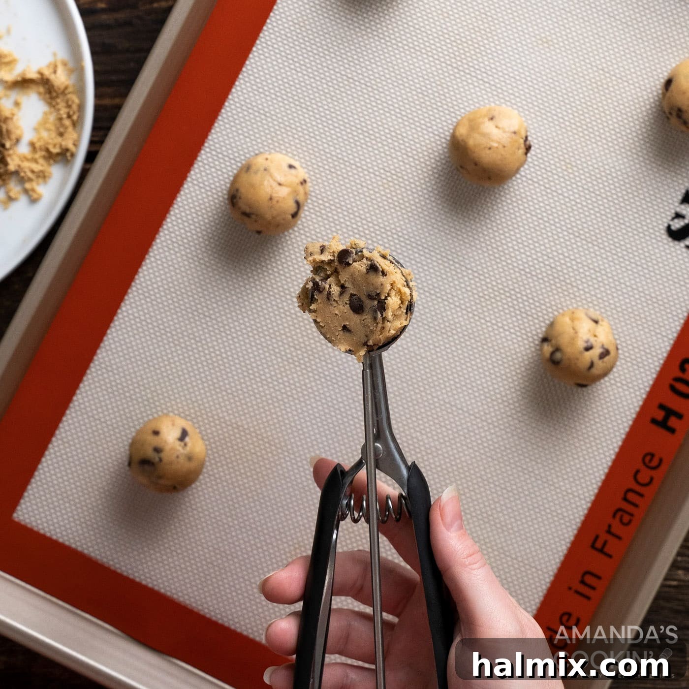 A scoop of chocolate chip cookie dough placed on a baking sheet lined with parchment paper, ready for baking.