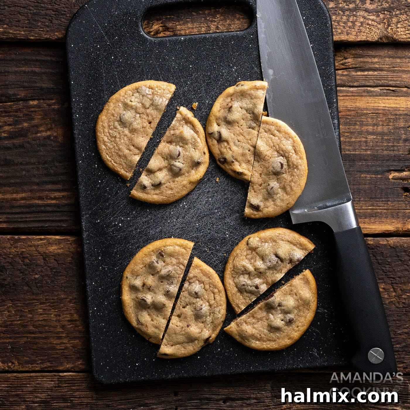 A chocolate chip cookie carefully cut in half, with one half already spread with red frosting, demonstrating the first step of assembly.