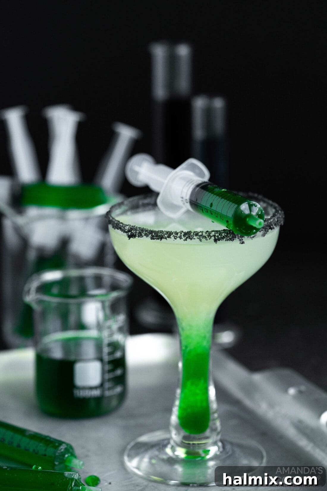A vibrant green Frankenstein Margarita, perfectly crafted, sits on a dark platter, ready for a Halloween party. The glass rim is coated with black lava salt, and a subtle lime garnish adds to its allure.