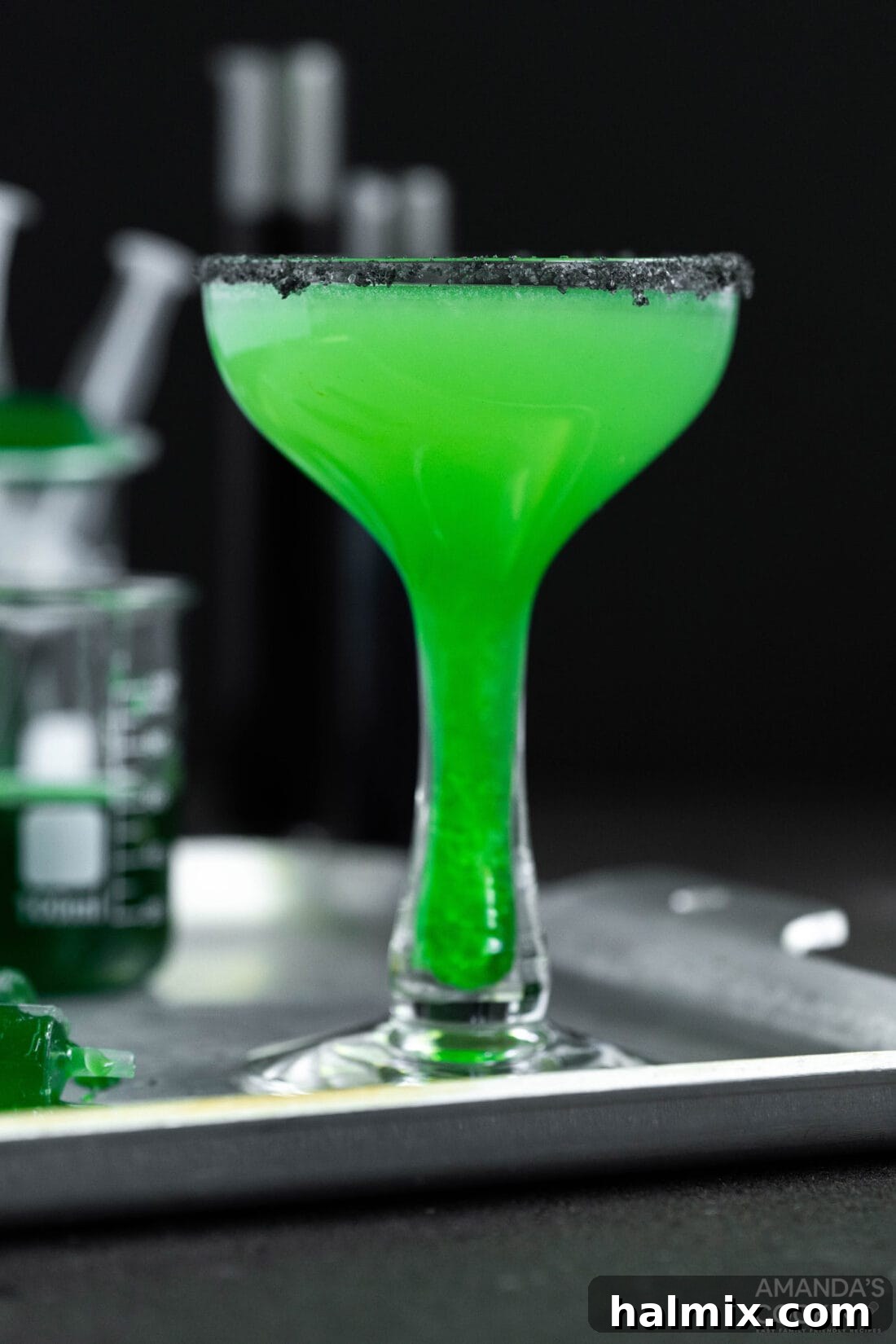 A close-up shot of the Frankenstein Margarita, showcasing its mesmerizing green color and the dramatic black salt rim, with subtle hints of lime in the background.